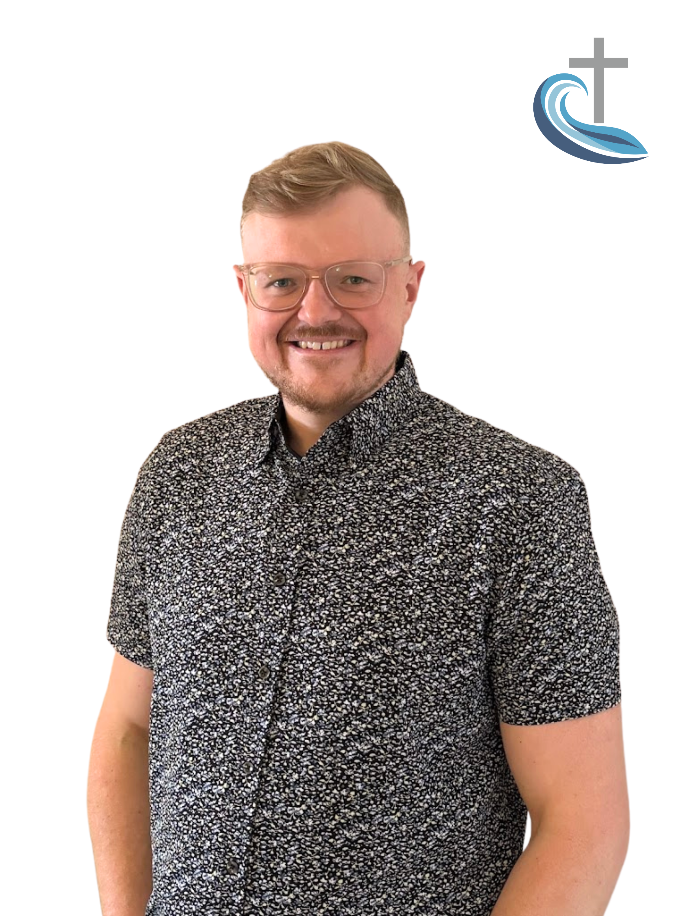A man with glasses and a short beard, smiling, wearing a black and white patterned shirt, standing against a white background with a small logo of a cross and wave in the top right corner.