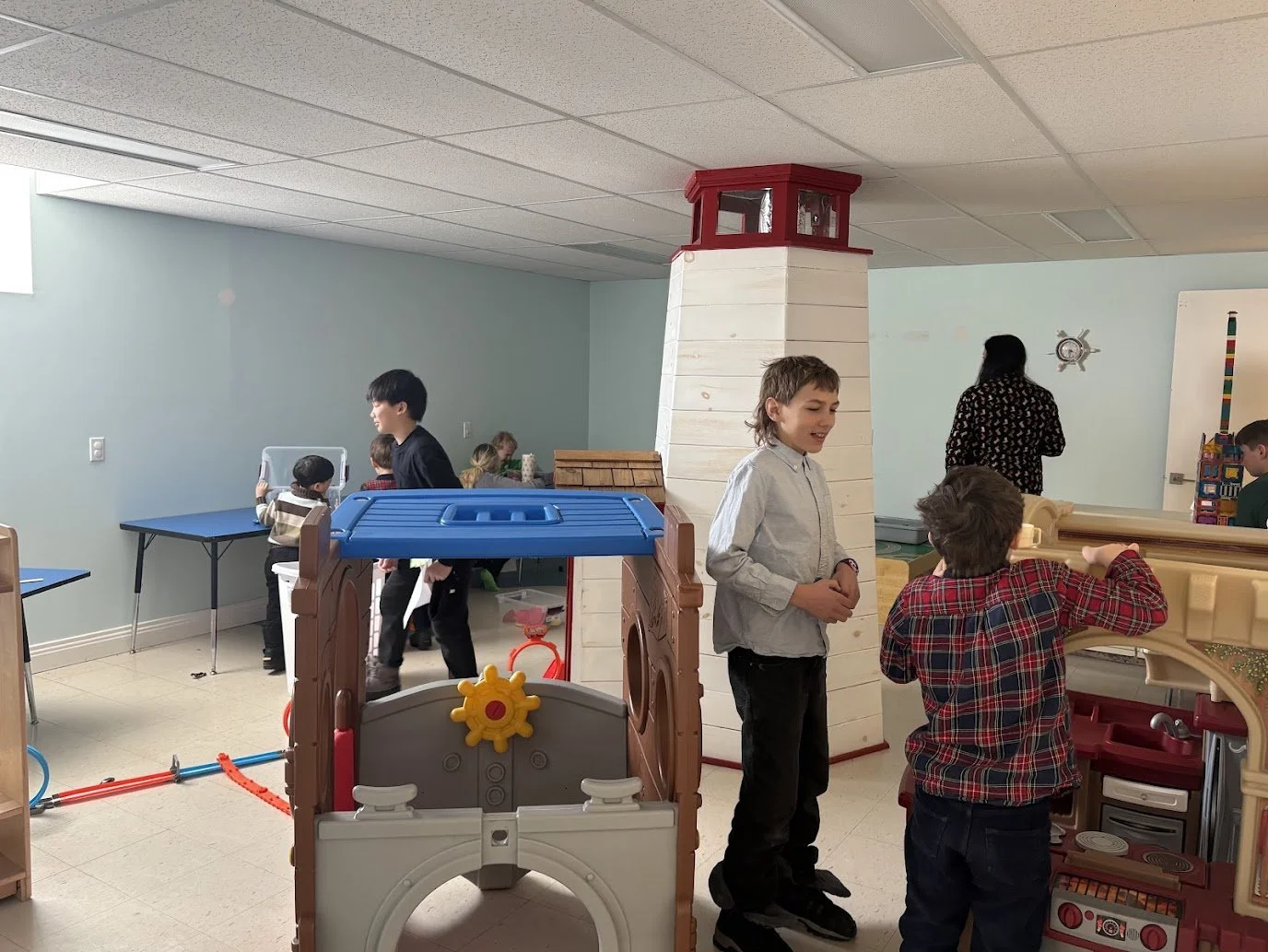 Children playing in an indoor play area with toys, activities, and a lighthouse-shaped structure.