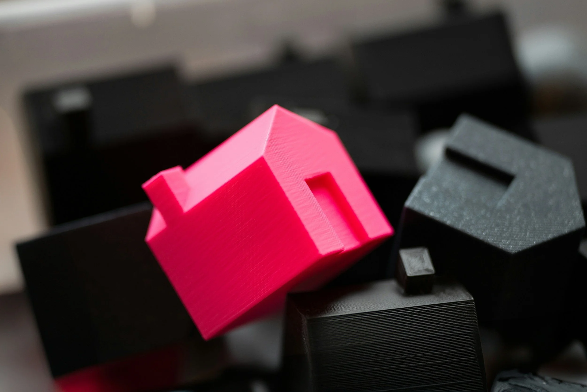 A pink 3D-printed house model placed on a black keyboard.