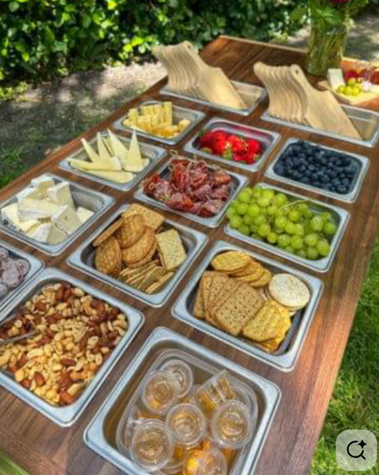 A cheese and fruit platter with nuts, crackers, grapes, blueberries, strawberries, and cheese varieties on a wooden table outdoors.