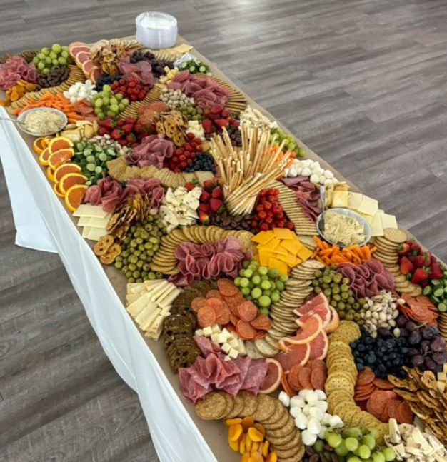 Large charcuterie board with various cheeses, meats, fruits, nuts, and crackers on a table.