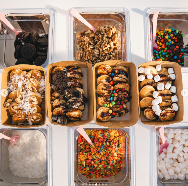Ice cream toppings in containers, including Oreos, caramel and walnuts, chocolate chips, multicolored sprinkles, mini marshmallows, shredded coconut, Fruity Pebbles, and mini marshmallows.