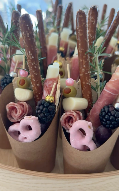 Close-up of savory snack cones filled with pretzels, cheeses, meats, blackberries, pink and white candies, and garnished with rosemary.