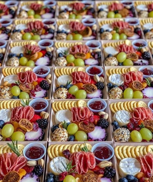 Multiple trays of assorted desserts, including grapes, cookies, berries, cheese, sliced meats, and small bowls of red jam.