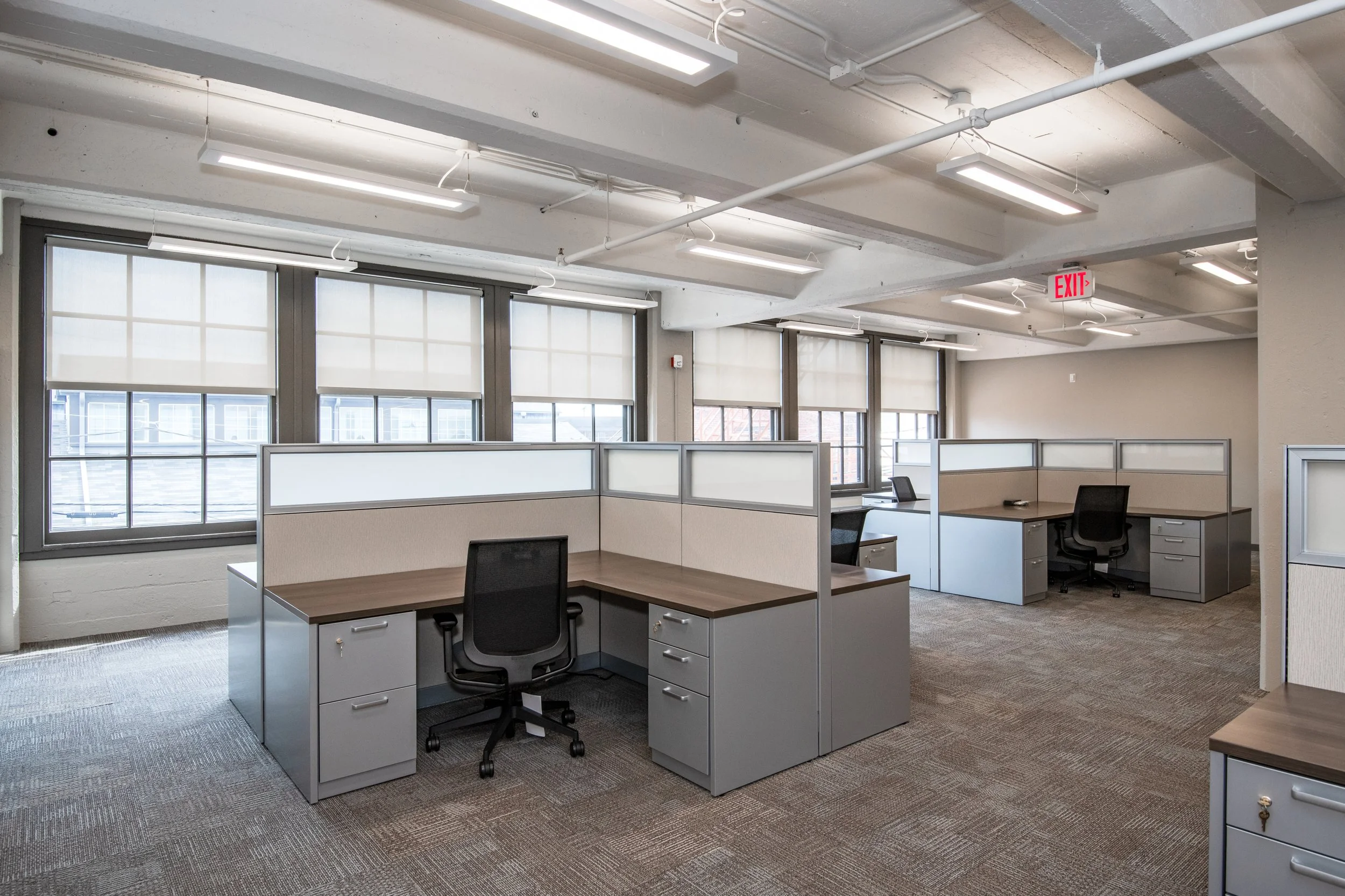 Open office floor plate at the Dayton Motor Car Building featuring workstation cubicles, carpeted floors, and natural light from original windows in a finished tenant suite in downtown Dayton, Ohio.