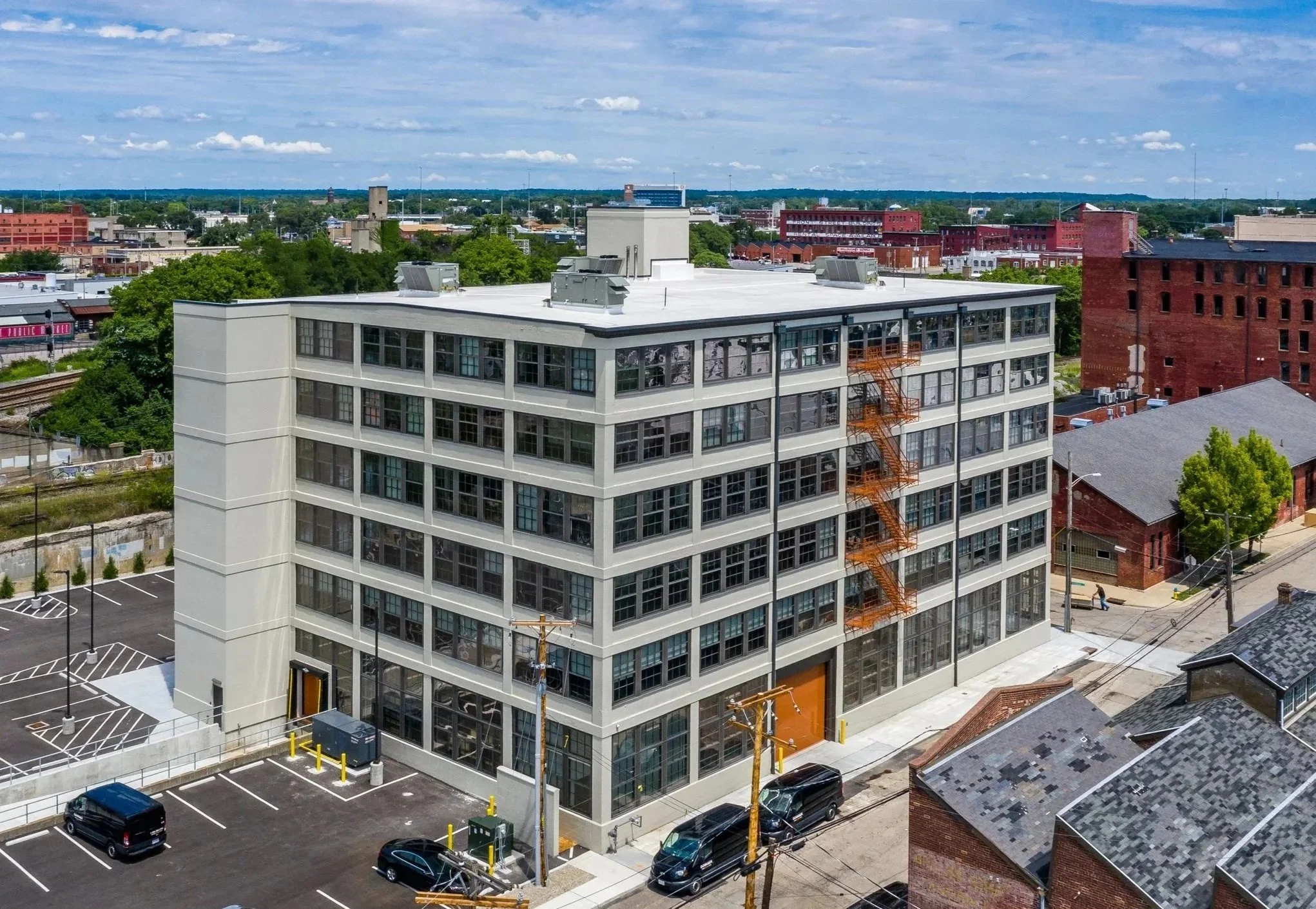 Aerial drone photo of the Dayton Motor Car Building exterior, a six-story historic industrial building with rows of large original multi-pane windows and a light grey facade, located at 15 McDonough St in the Oregon East District of downtown Dayton,