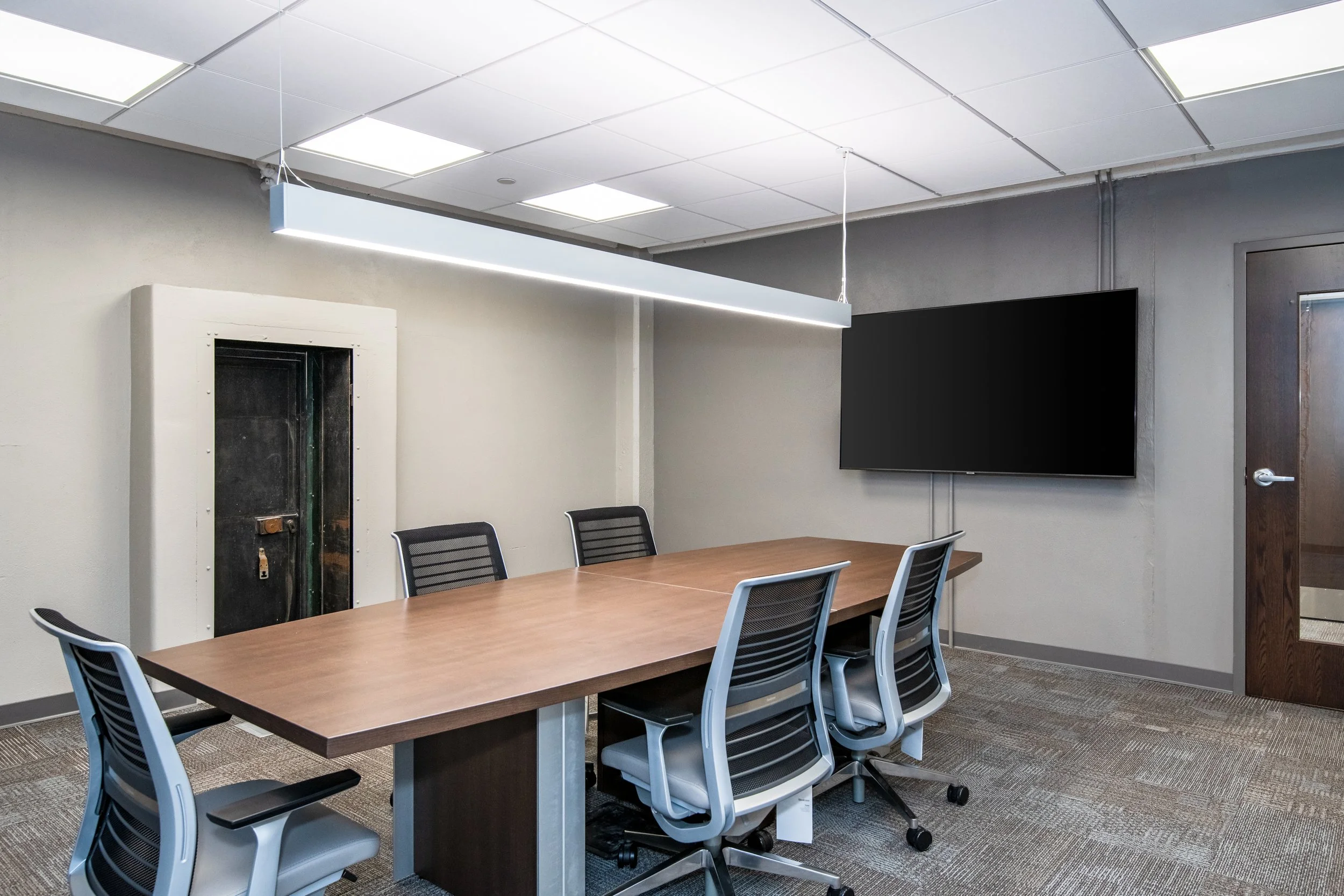 Modern conference room inside the historic Dayton Motor Car Building featuring a meeting table and chairs with exposed industrial ceiling details and natural light from original windows.