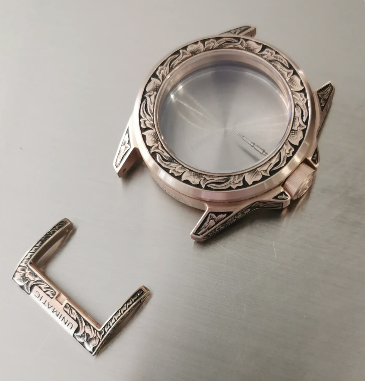 Cassa di uncorologio di lusso in bronzo con decorazioni incise senza cinturino, disposto su una superficie metallica