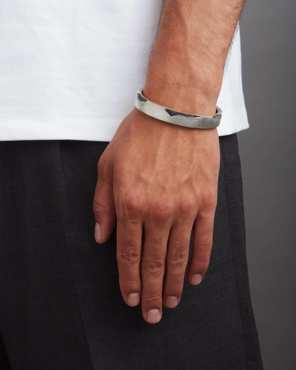 Mano con bracciale d'argento cuff con fratture ed erosioni incise, indossato sul polso destro, indossa una maglietta bianca e pantaloni neri