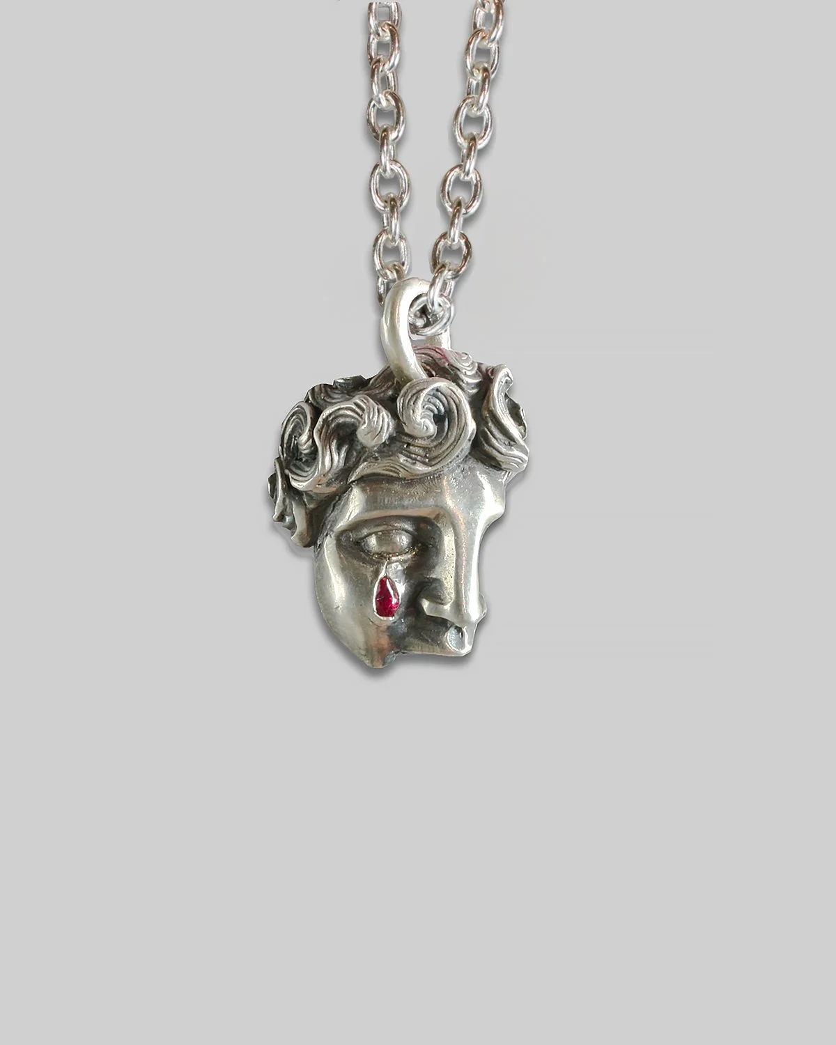 Collana con pendente IDOL in argento raffigurante un frammento di volto di Apollo in argento con rubino a goccia incastonato. 