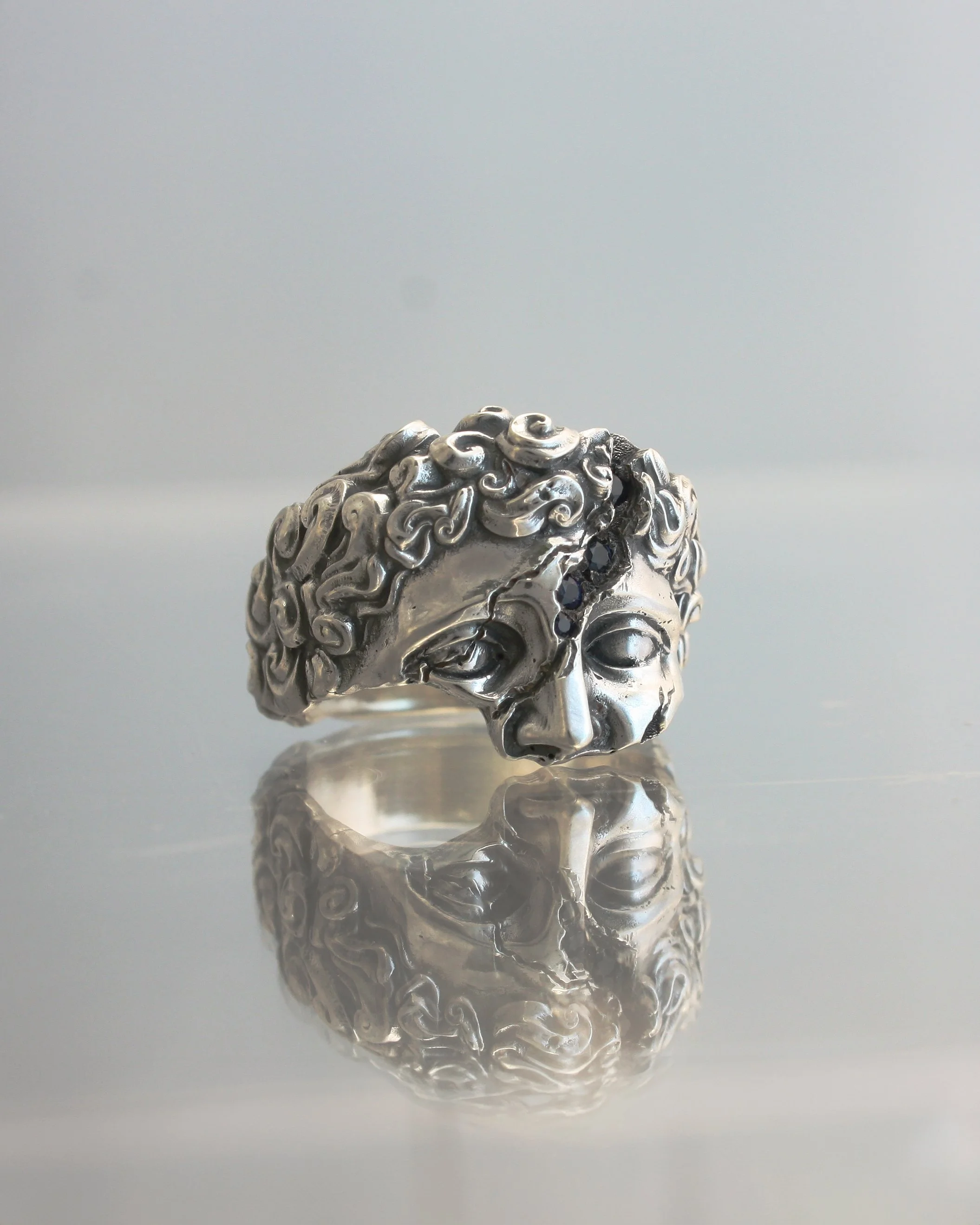 Anello IDOL in argento con volto scultoreo stile classicista, lavorazione erosa e incastonatura zaffiri.