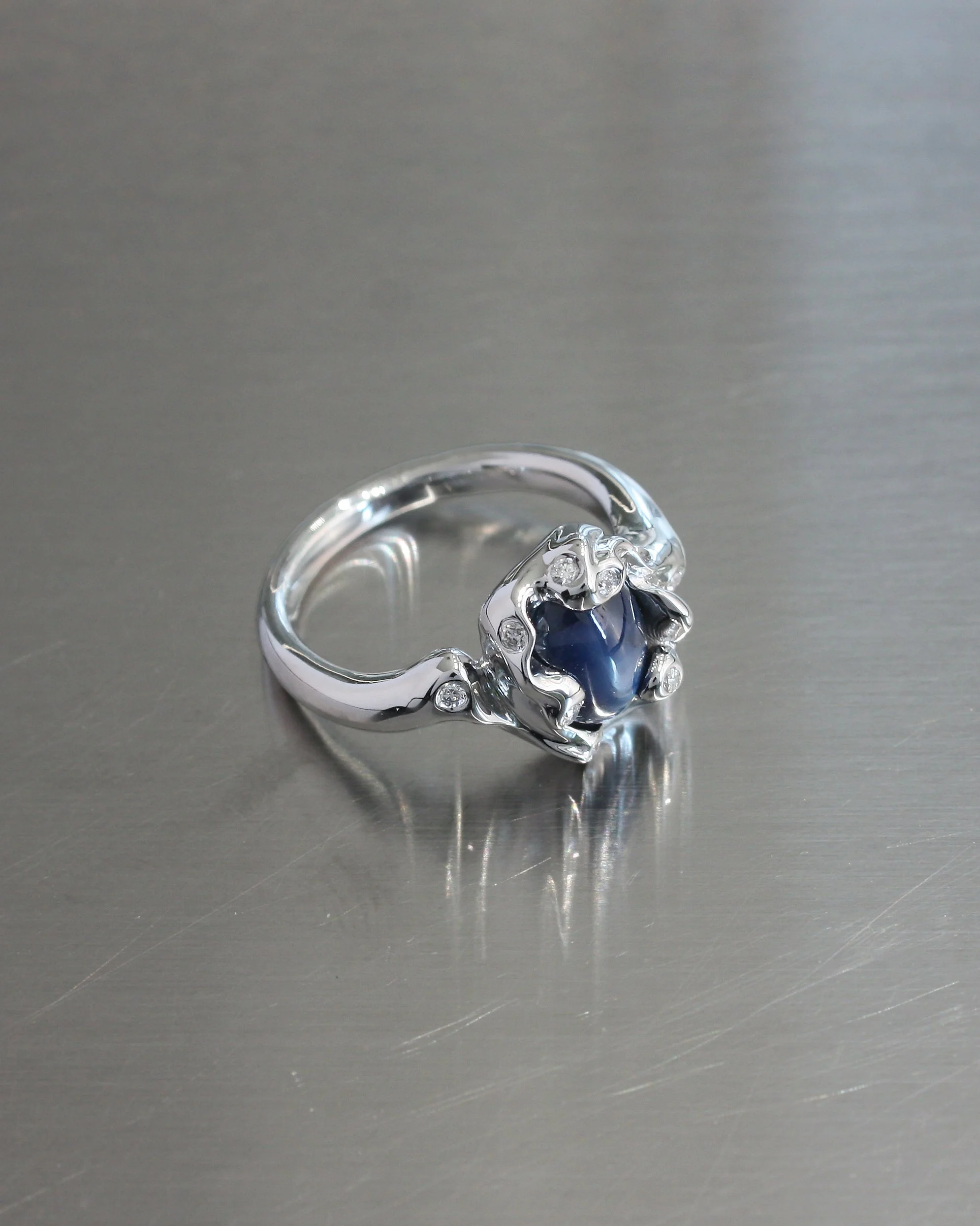 Engagement ring ELL milano in oro bianco, zaffiro stellato e diamanti, pezzo unico su misura, posizionato su superficie in inox. anello da fidanzamento alternativo.