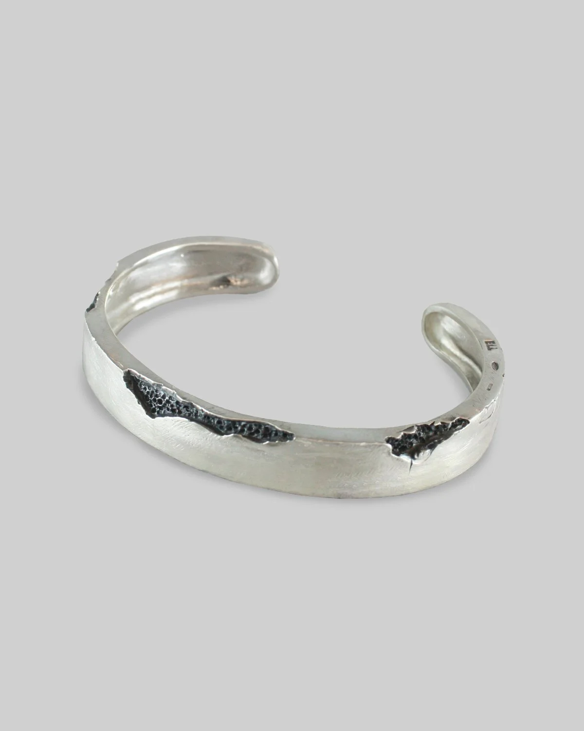 Bracciale cuff in argento con dettagli neri erosi incisi e superficie opaca, aperto e semi-circolare.