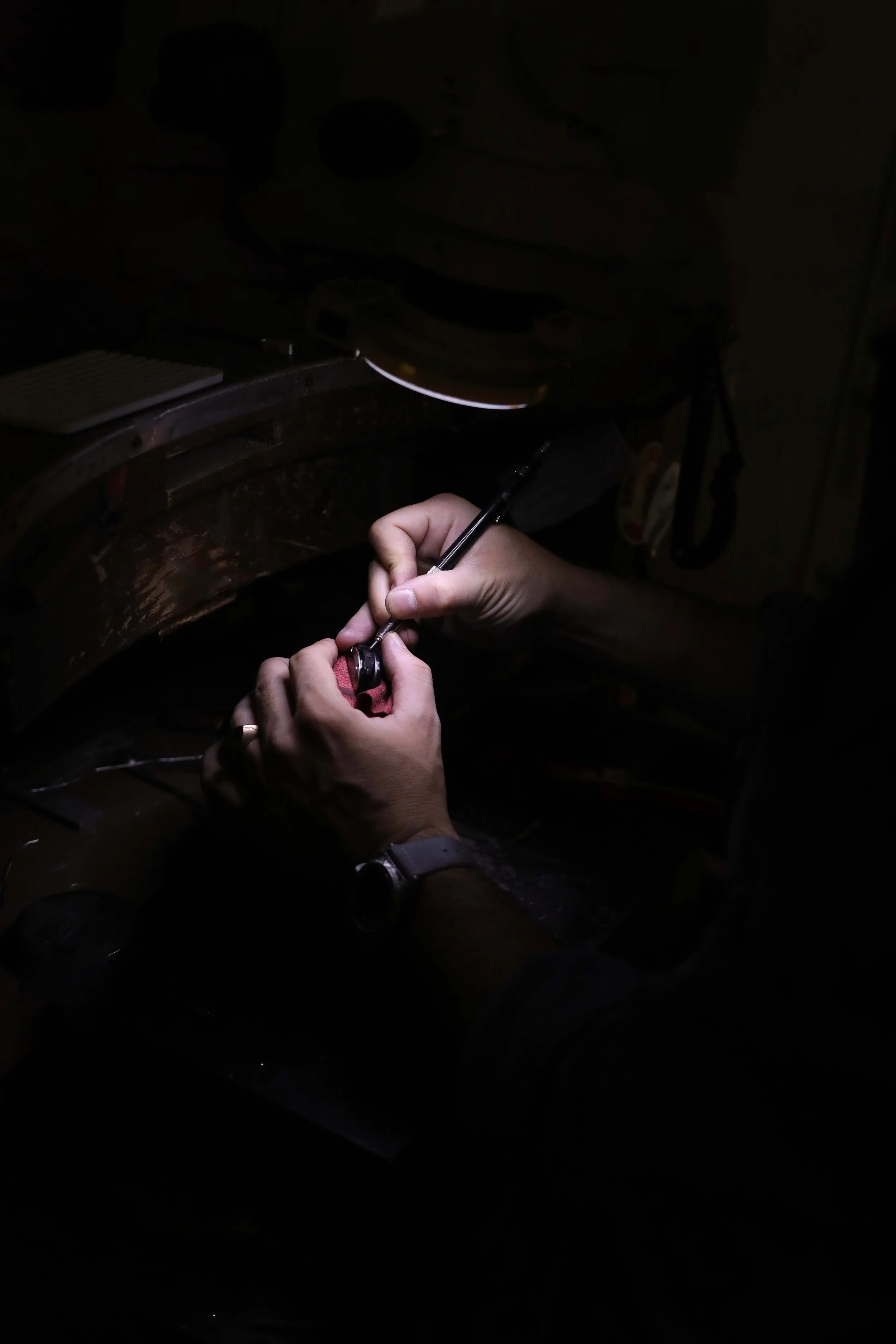 Mani che lavorano con strumenti di precisione in un ambiente oscurato. L'illuminazione centrata sulle mani evidenzia le azioni di lavorazione.