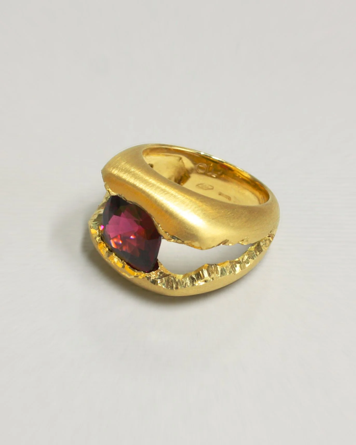 Anello pezzo unico in oro 18kt satinato con grossa rodolite naturale taglio cushion invastonata in sospensione, fotografato su sfondo neutro.