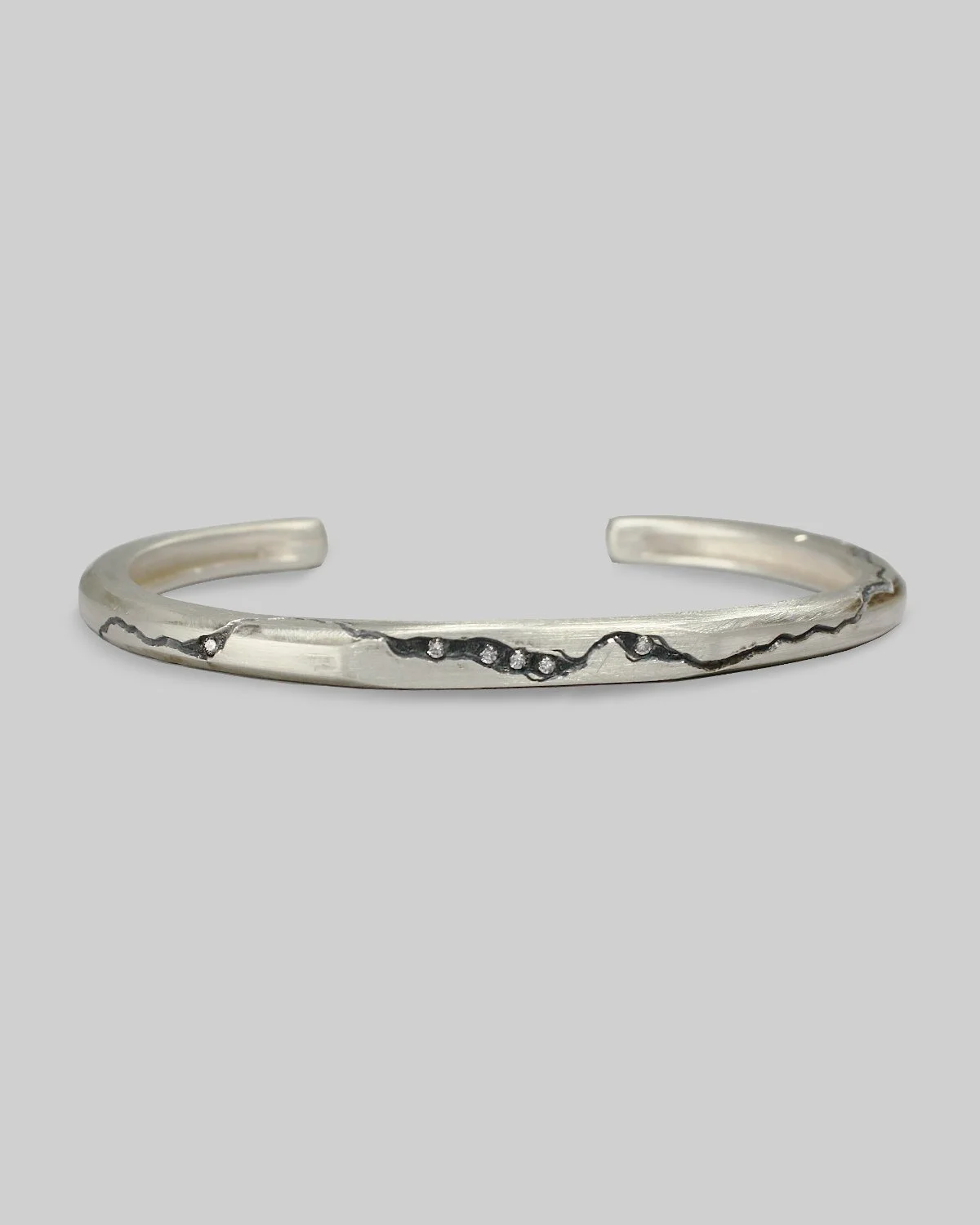 Bracciale cuff in argento rigido, con frattura incisa a mano e diamanti incastonati all'interno, fotografato su fondo neutro.