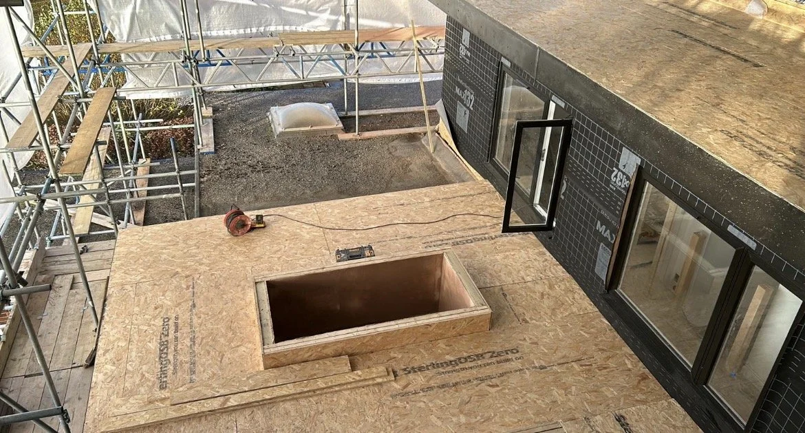 Construction site with plywood flooring, scaffolding, open windows, and building materials.