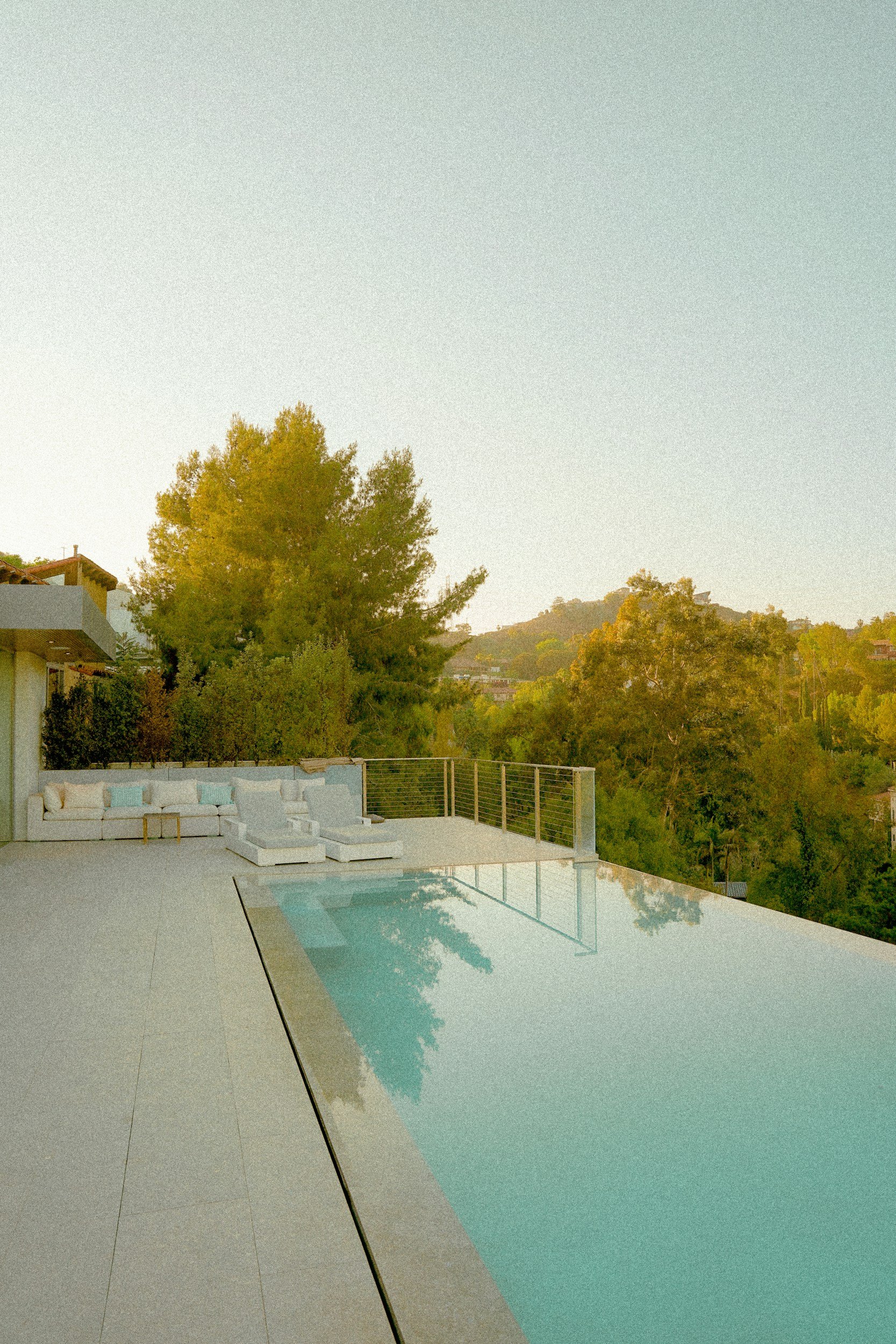 Empty swimming pool on a patio with outdoor lounge chairs, overlooking trees and hills.