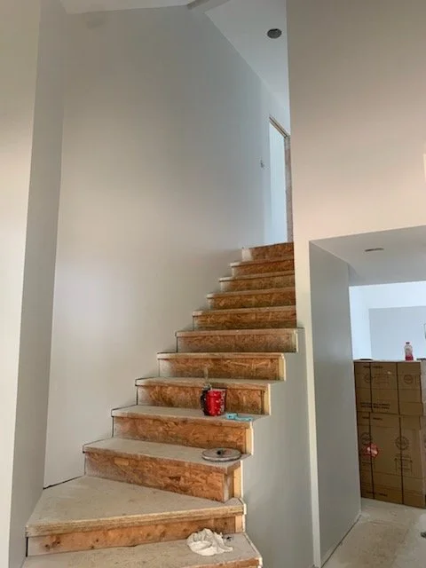 Interior of a house under construction with a staircase in progress, showing wooden steps and some construction materials on the steps.