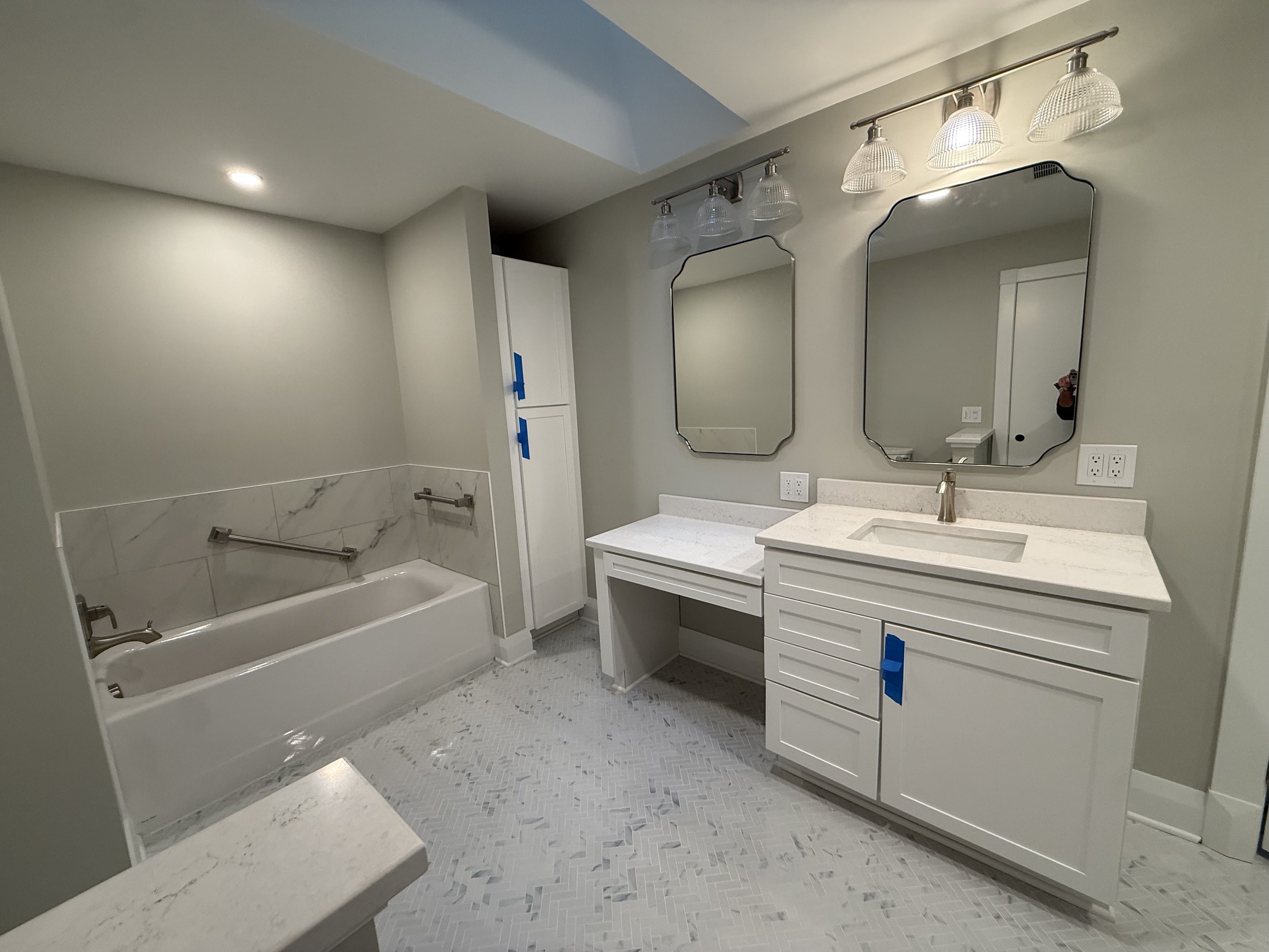 A modern bathroom with a bathtub, dual mirrors, a vanity with a sink, and new light fixtures.