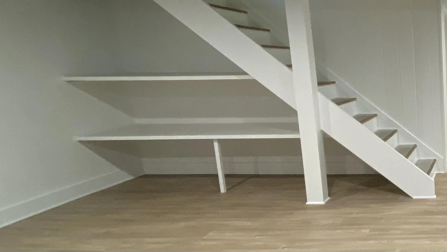 Empty white built-in staircase with open risers in a room with light-colored flooring and white walls.