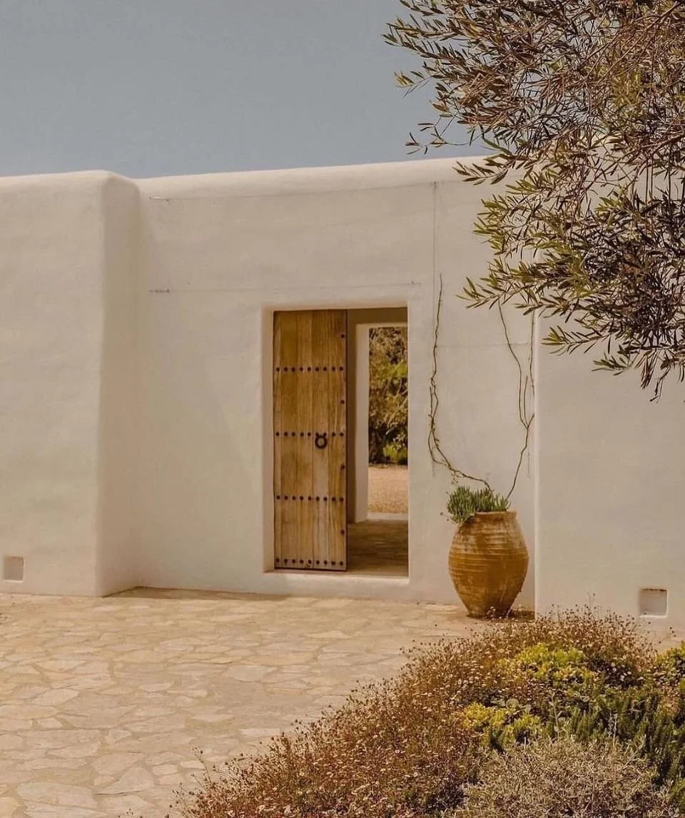 Minimal whitewashed Mediterranean home with natural wood door, stone flooring and olive tree landscape.