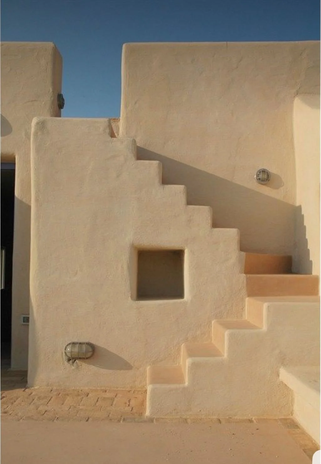 Minimal Mediterranean architecture with sculptural whitewashed stairs, textured plaster walls and warm natural light.