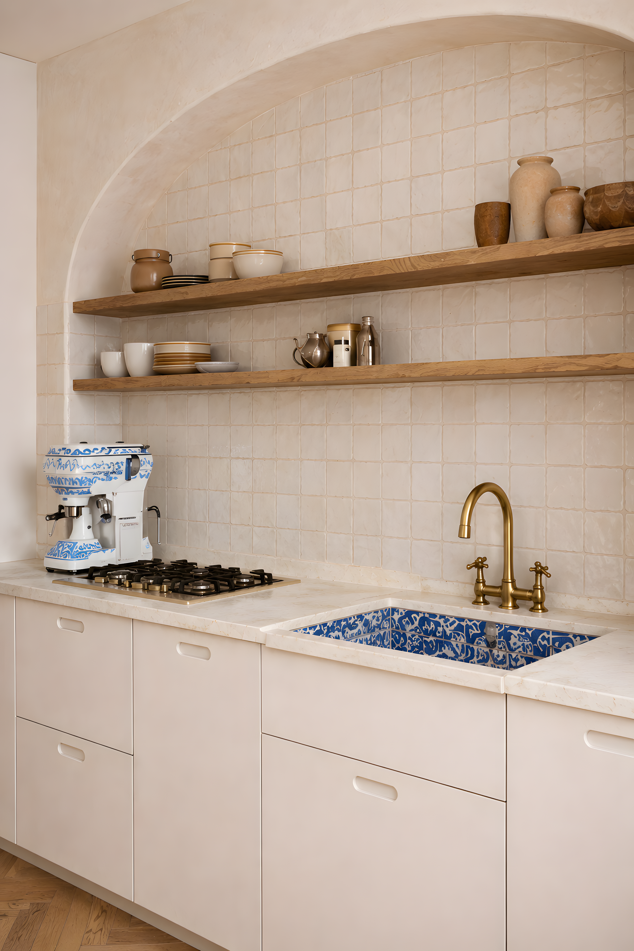 Close-up of Mediterranean-inspired kitchen with handcrafted cream tiles, oak shelving, brass tapware and blue ceramic sink detail in Milan apartment.