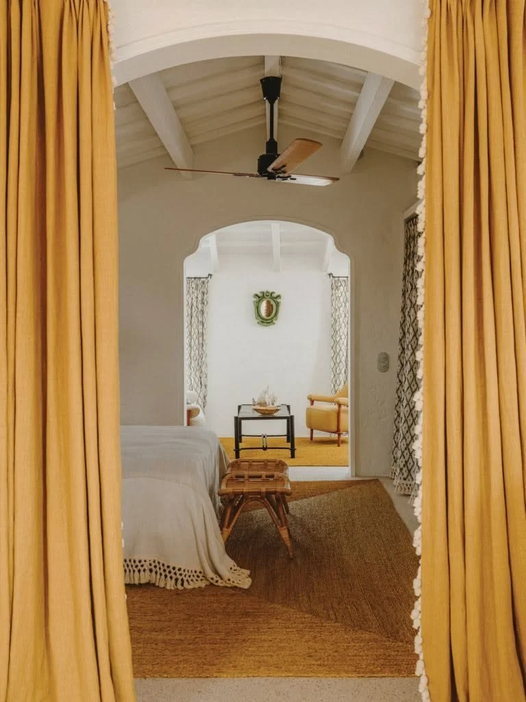 Warm Mediterranean bedroom with arched openings, mustard linen curtains, woven textures and soft natural light.