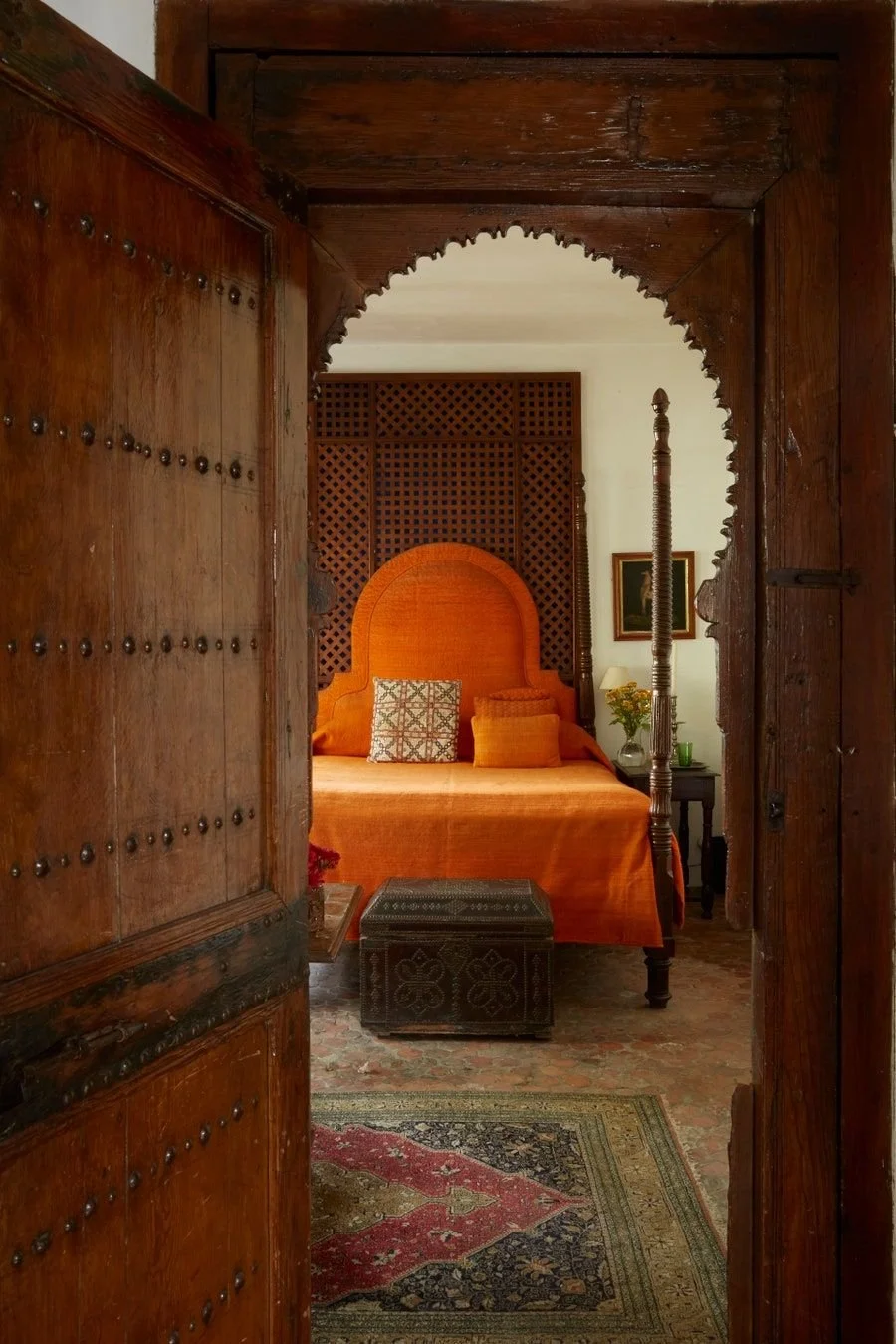 Traditional Tangier riad bedroom with carved wooden doors, terracotta-orange textiles and Moroccan architectural detailing.