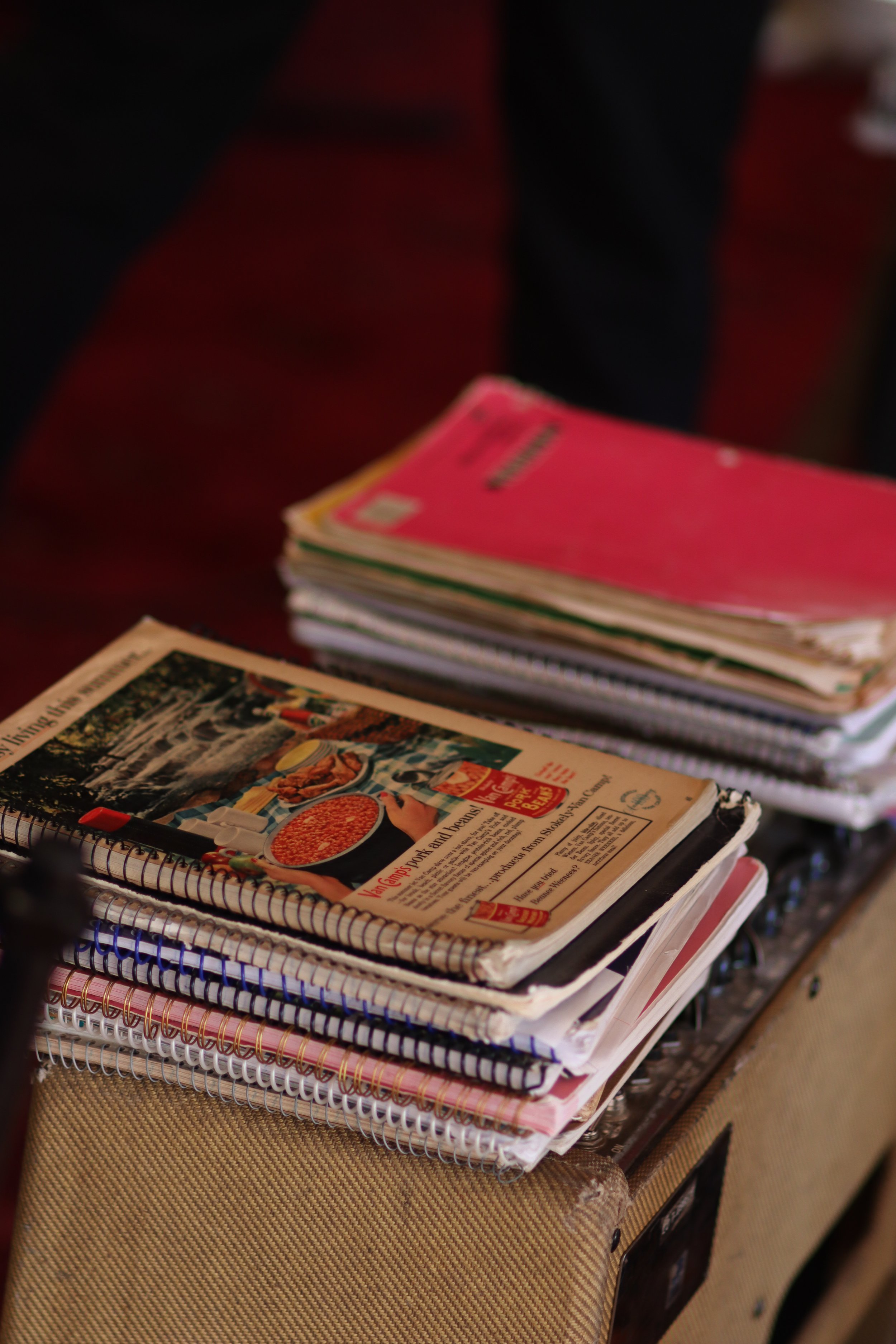 Stack of notebooks and magazines on a wicker surface, with some pamphlets visible on top.