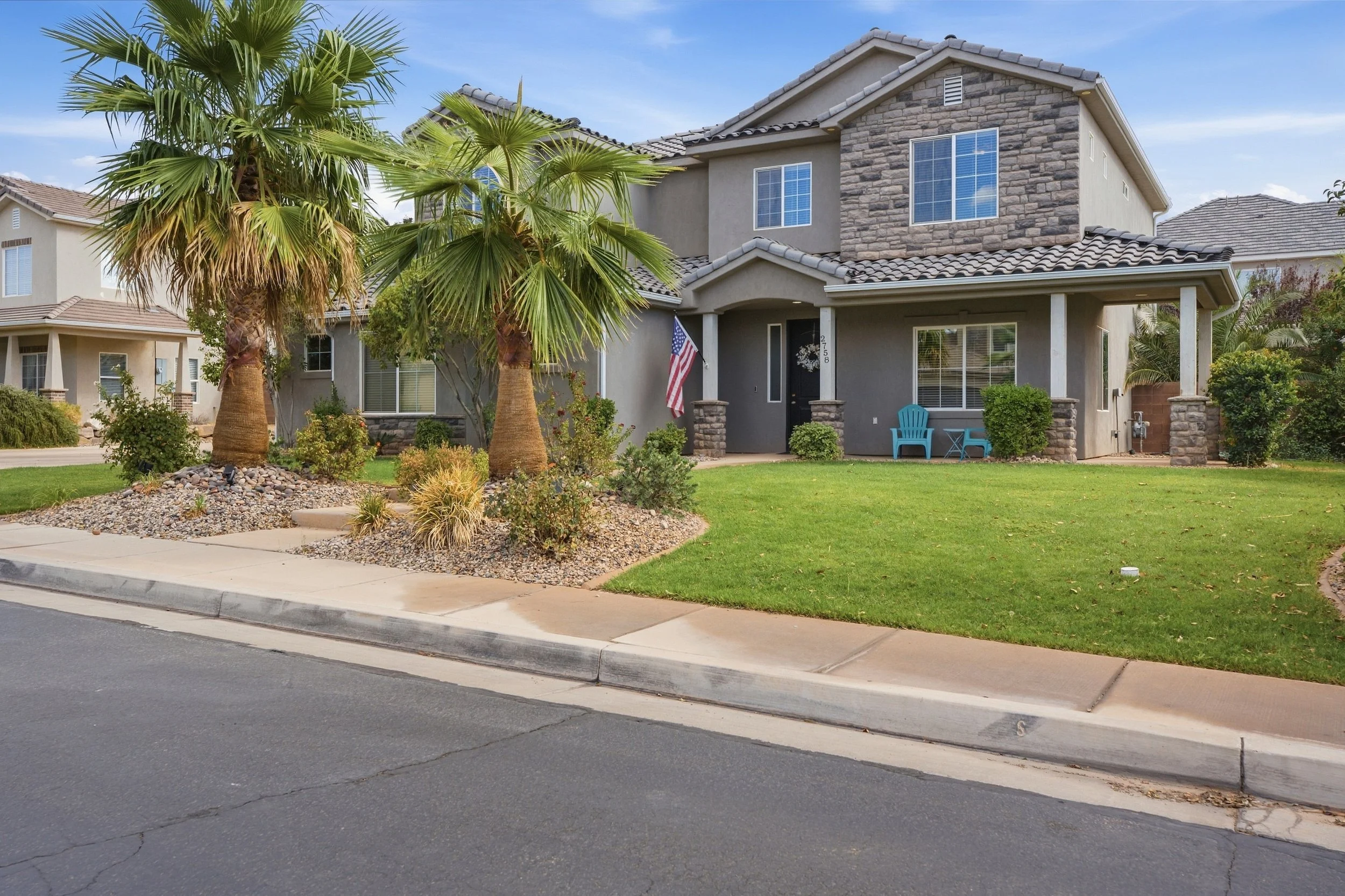 Front exterior of a two-story home with stone accents, palm trees, and a green lawn on Auburn Circle, St. George UT