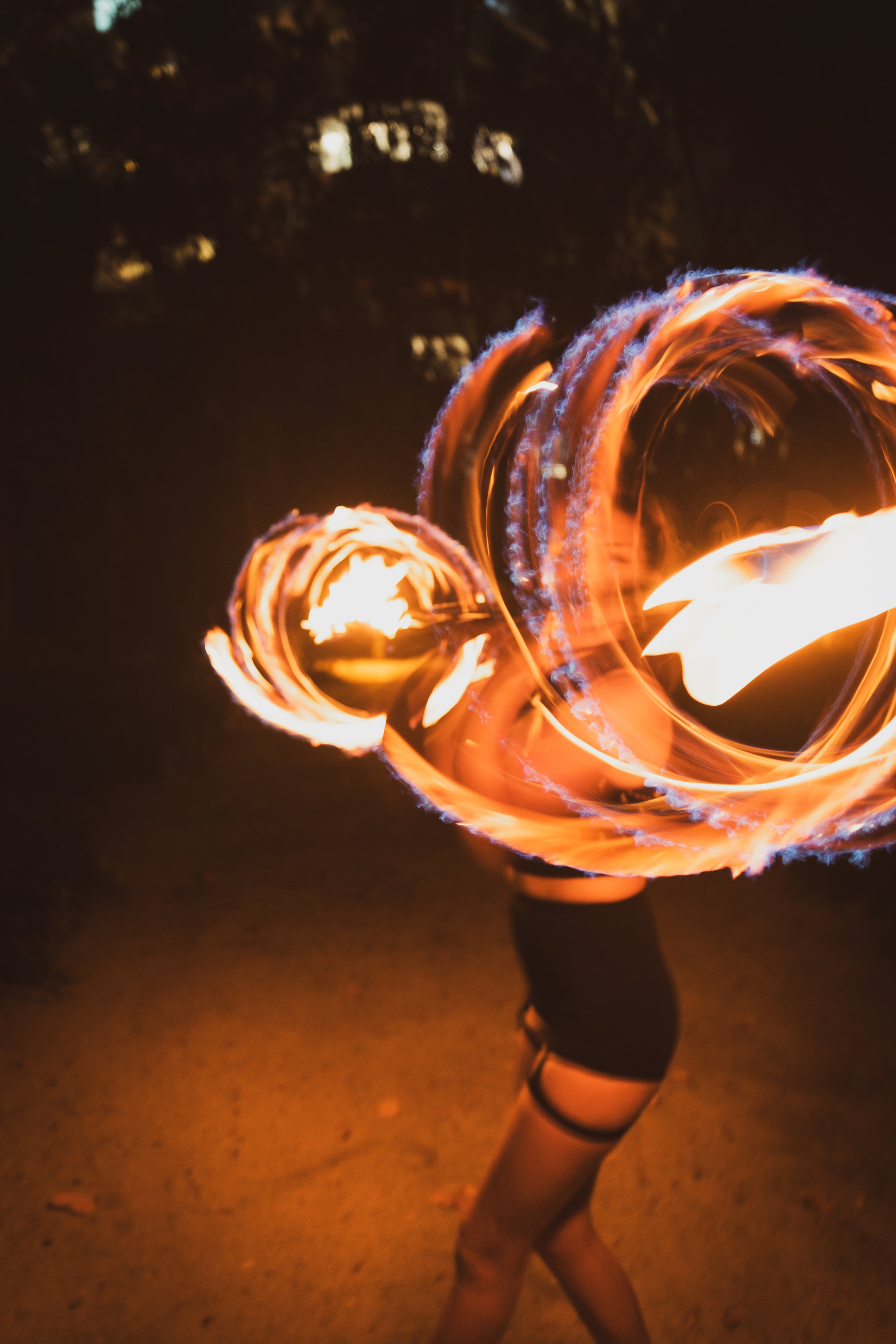 Person performing a fire spinning dance at night, with swirling flames creating circular patterns.
