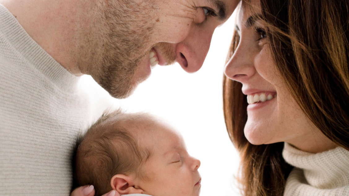 Close-up of a smiling couple looking at their sleeping newborn baby.