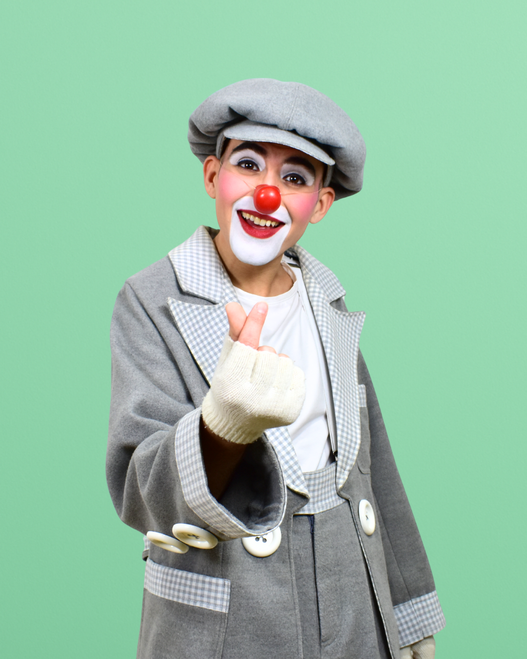 Payaso con maquillaje y gorra gris hace un gesto de aprobación en fondo verde