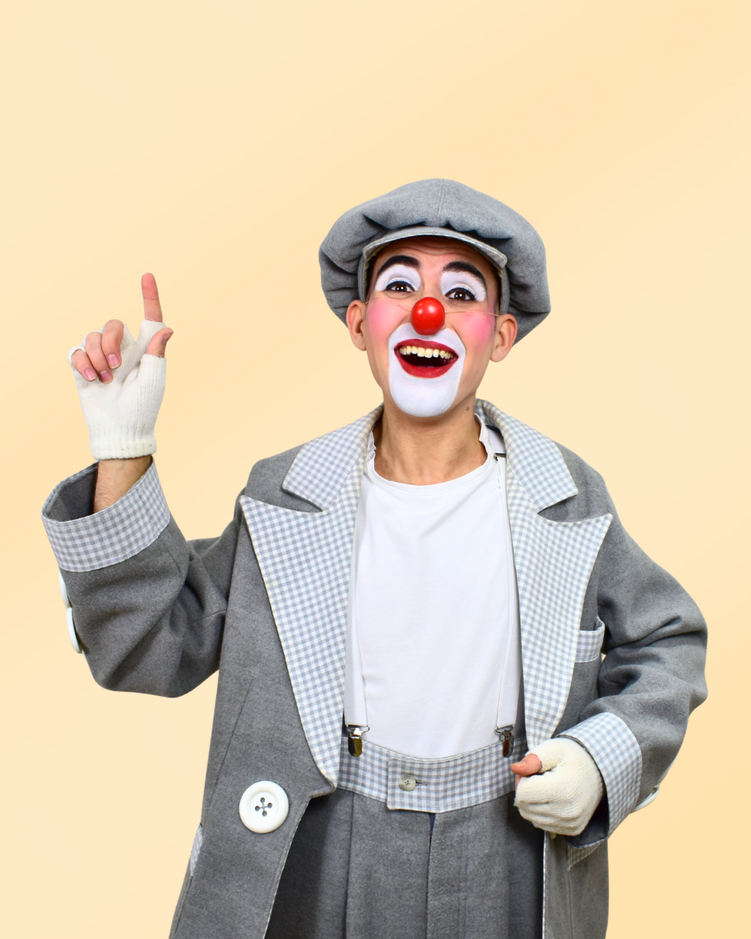 Payaso con nariz roja, maquillaje blanco en la cara, vestido de payaso y gorro gris, sonriendo y levantando un dedo