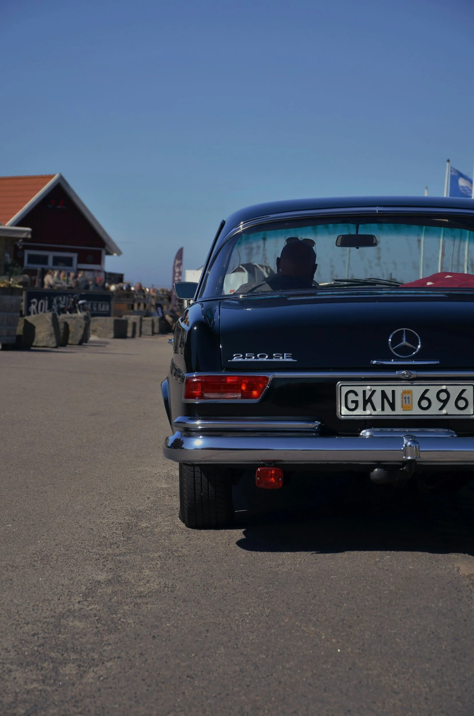 Rear view of a classic black Mercedes-Benz 250 SE parked outdoors during daytime, with a person visible through the windshield.