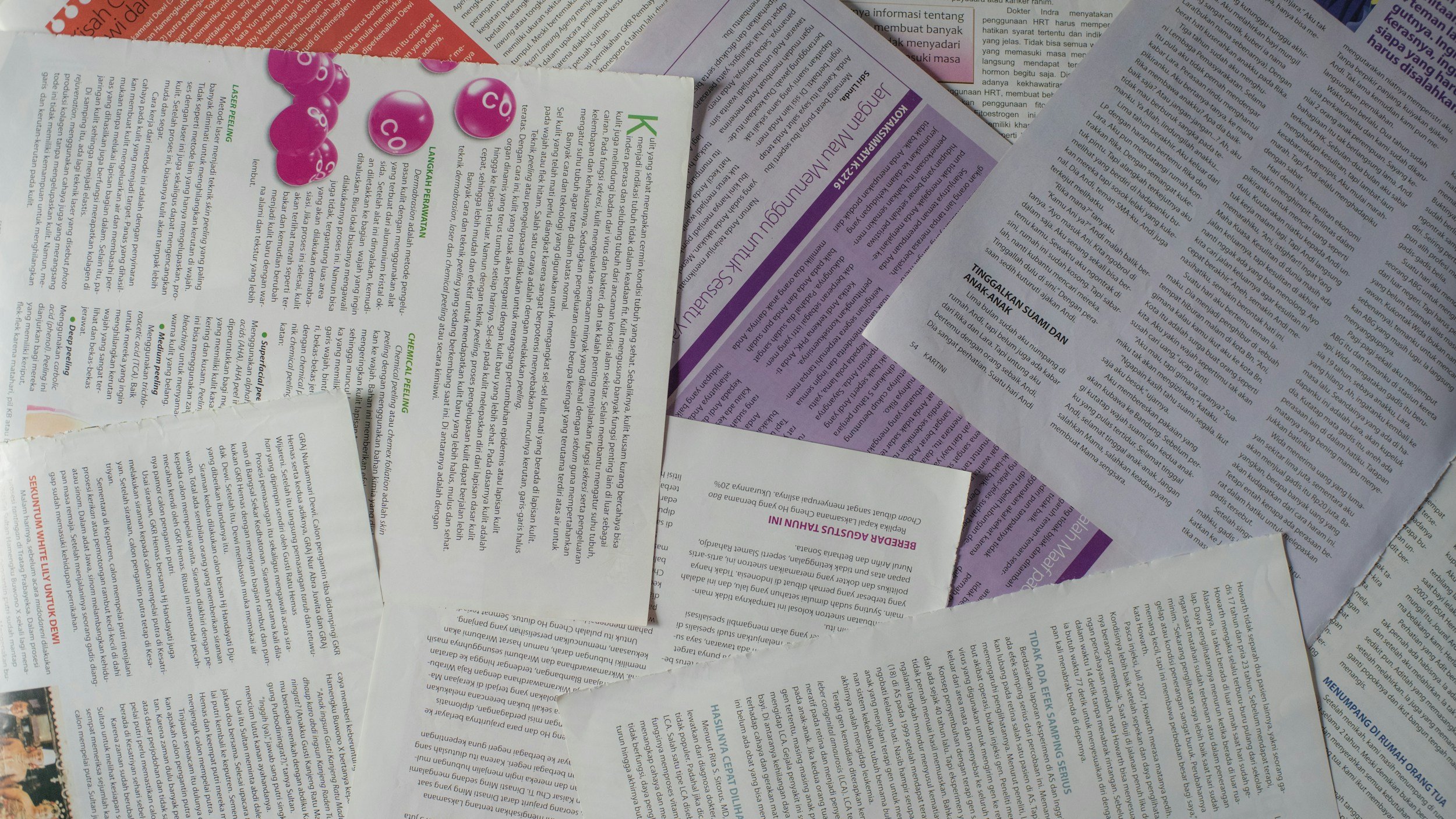 A scattered pile of various printed pages and flyers with different colors and text, including purple, green, and black, on a flat surface.