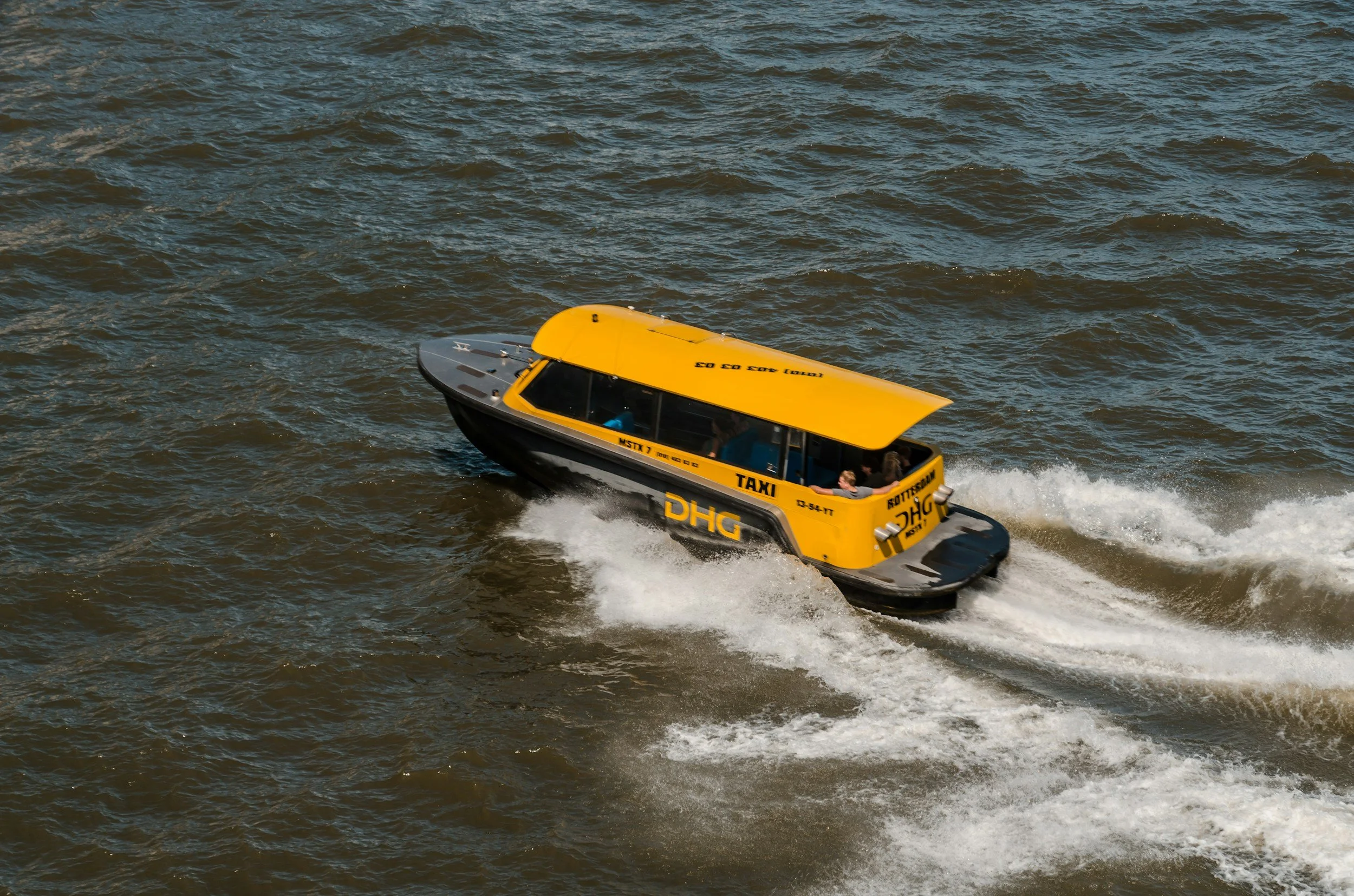 A yellow and black water taxi boat speeding on choppy water, with the words 'TAXI' and other markings visible on its side.