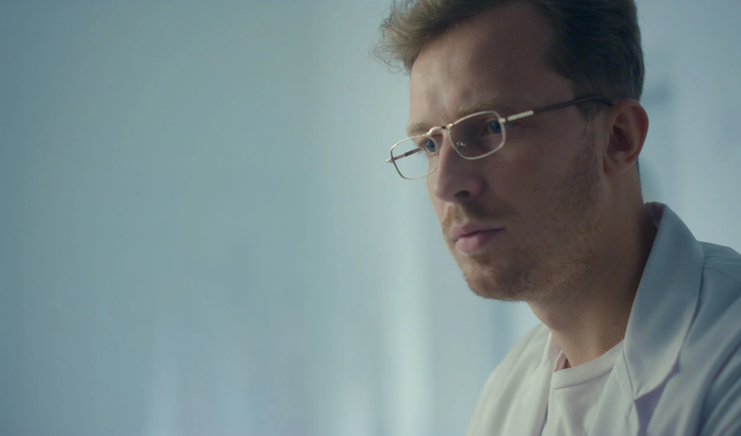 A focused male healthcare professional wearing glasses and a white coat in a clinical setting.