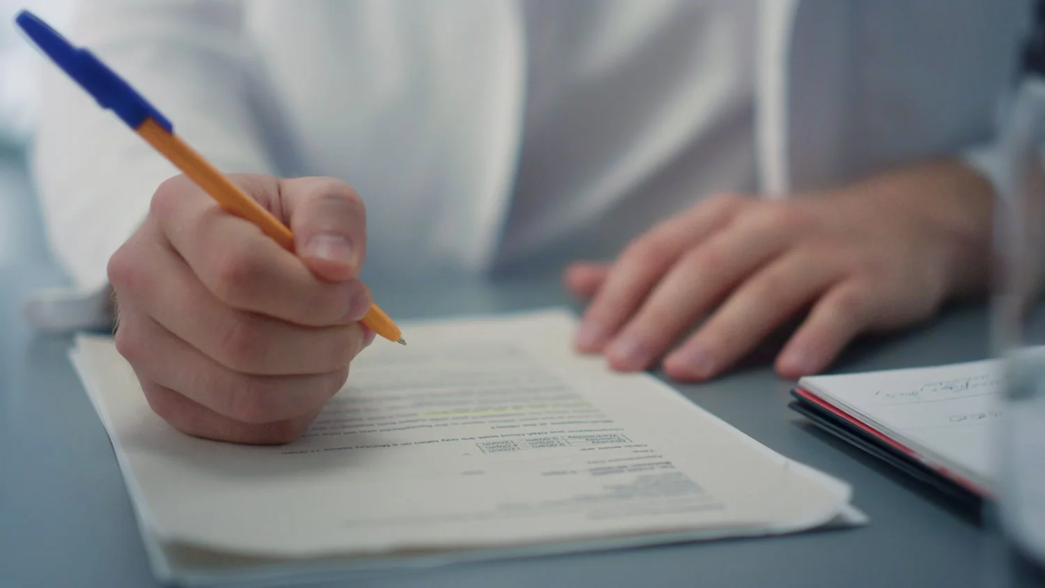 Close-up of a professional's hands writing notes on a medical form.