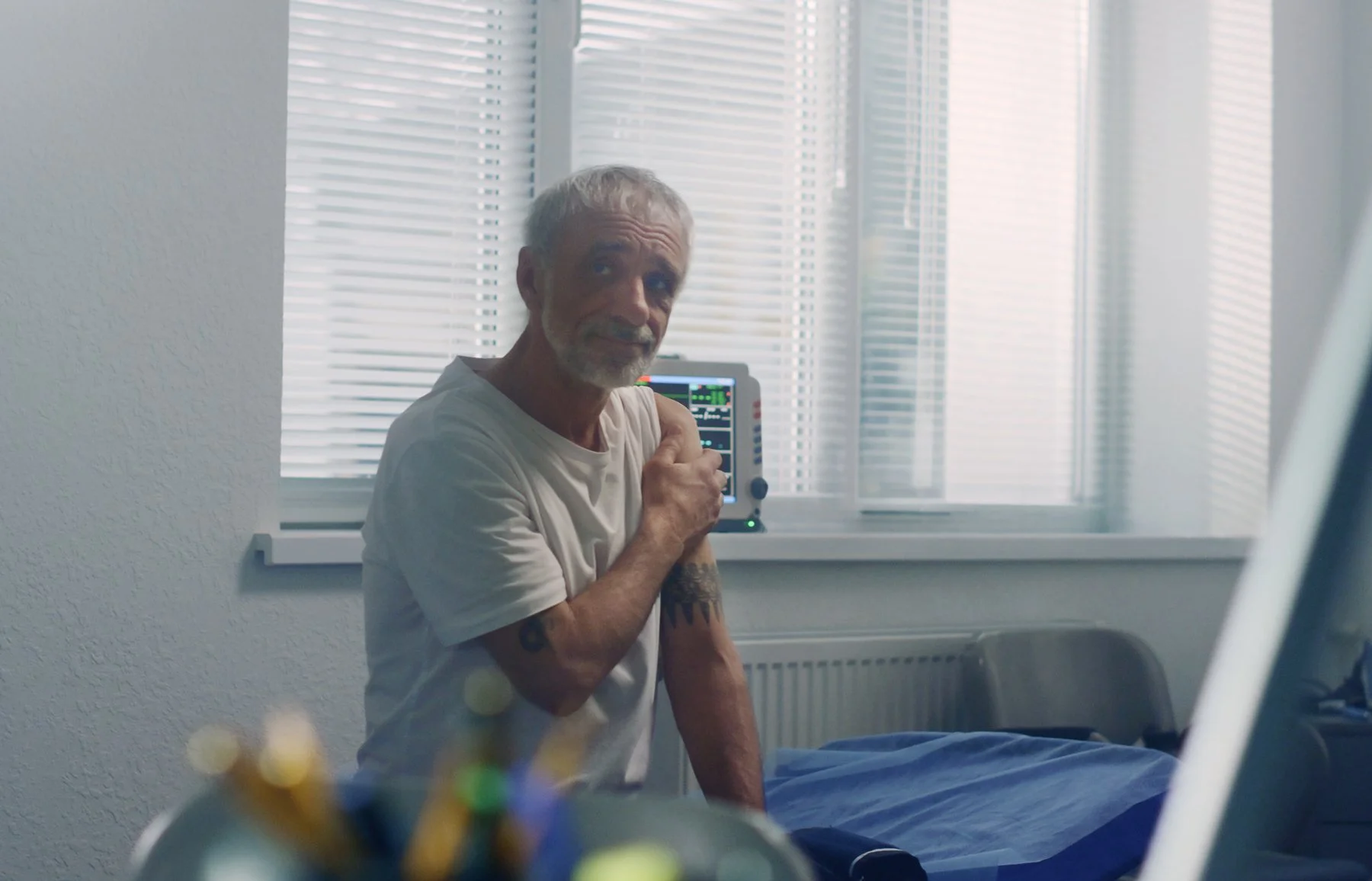 An older male patient sitting calmly in an exam room while receiving care from a provider.
