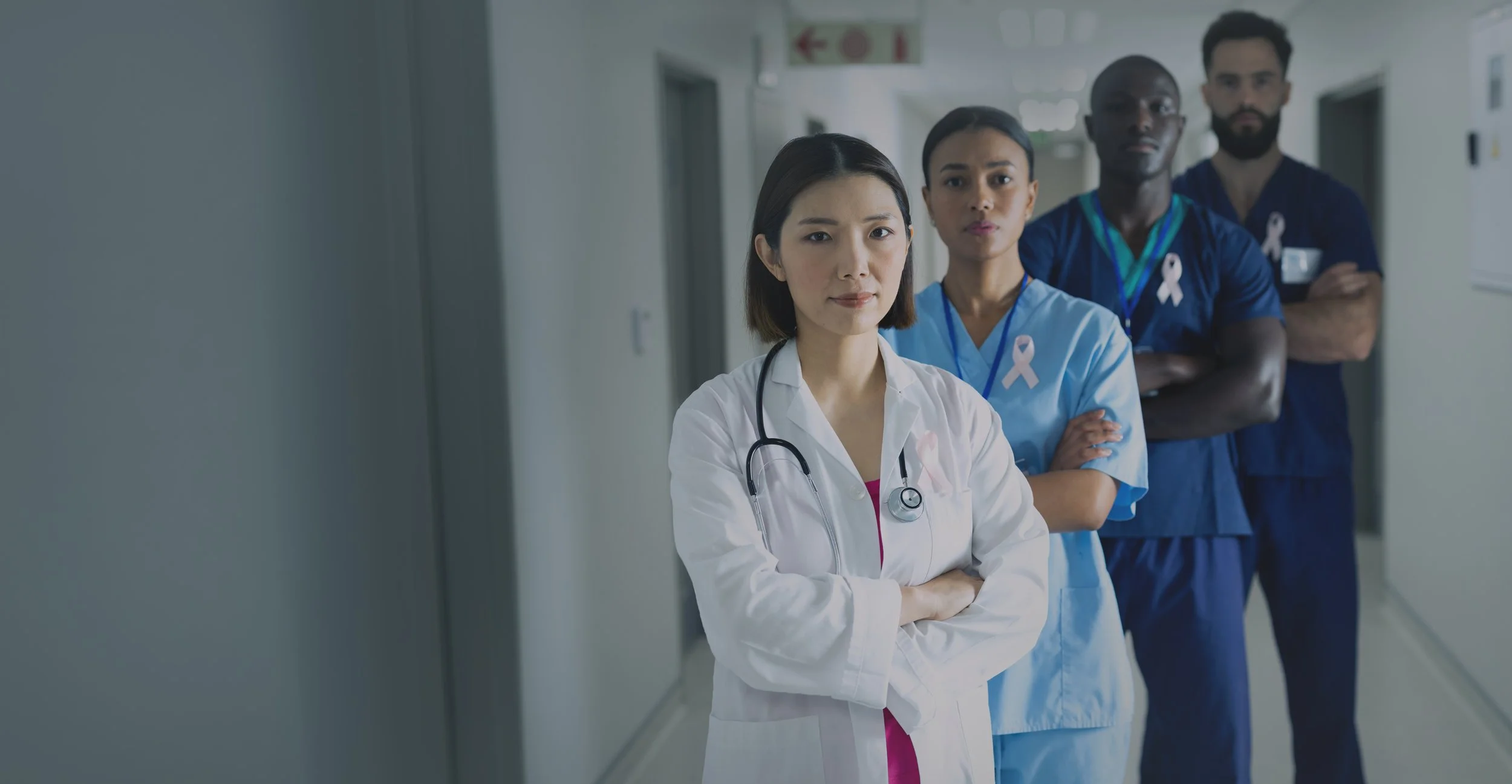 A diverse team of four healthcare professionals standing confidently together in a secure facility hallway.