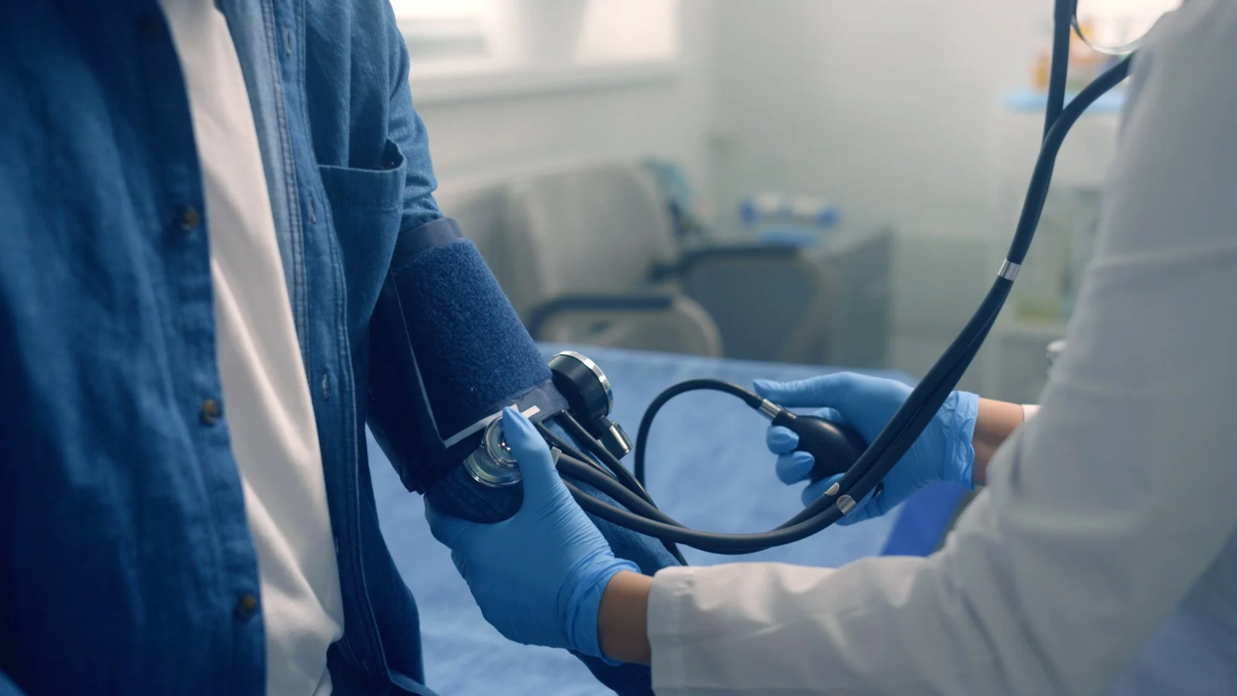 A healthcare provider's hands checking a patient's blood pressure with a cuff and stethoscope.