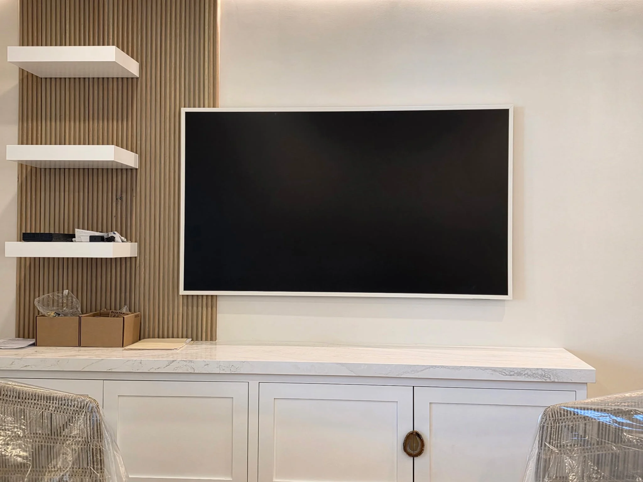 Reed paneling accent with floating shelves in home entertainment center, complimentary cabinetry below, and floating television bracket.