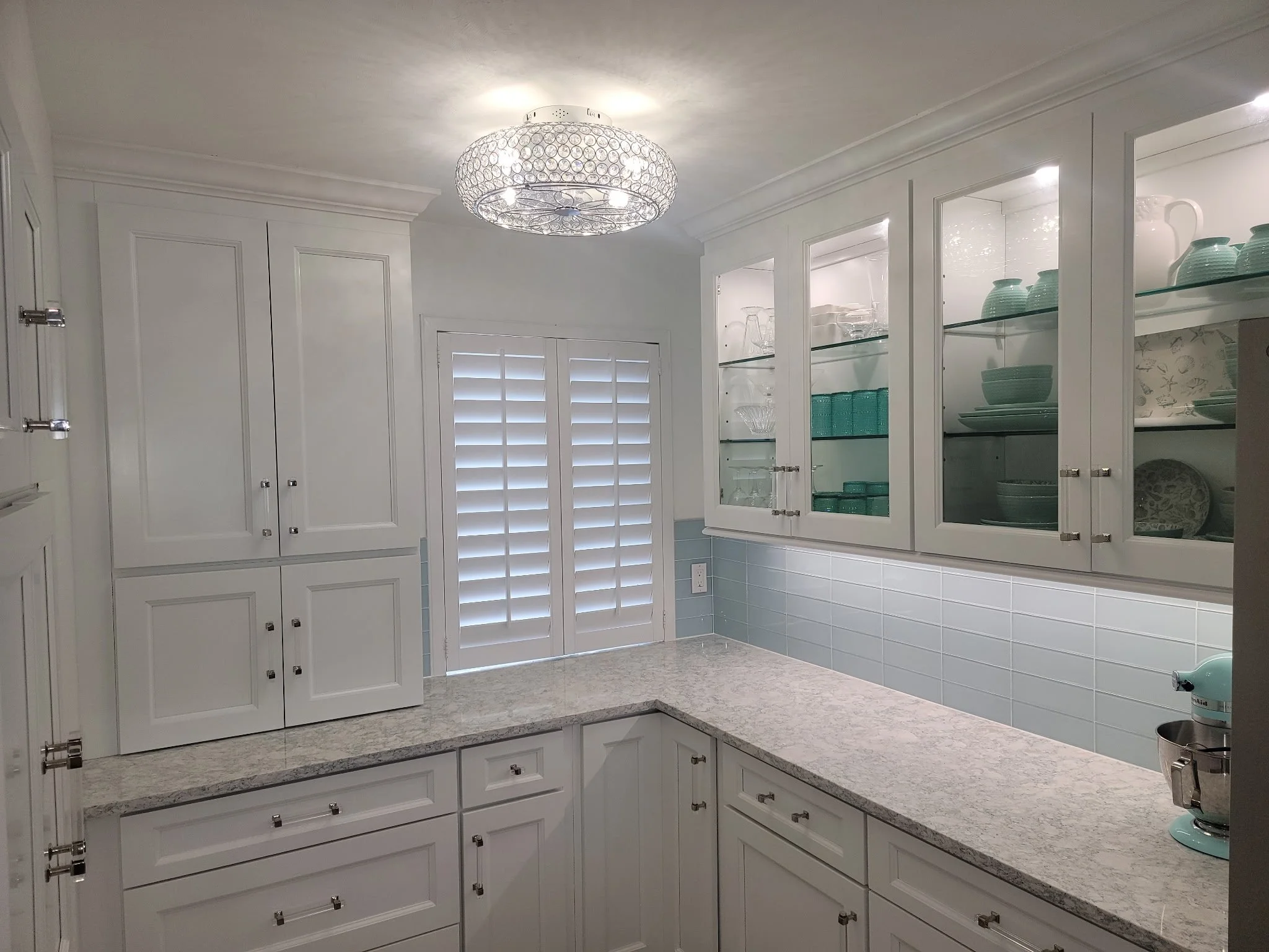 white kitchen cabinets with glass door panels, with decorative aqua colored dishes inside.  Clear glass light cover.  Quartz countertop.