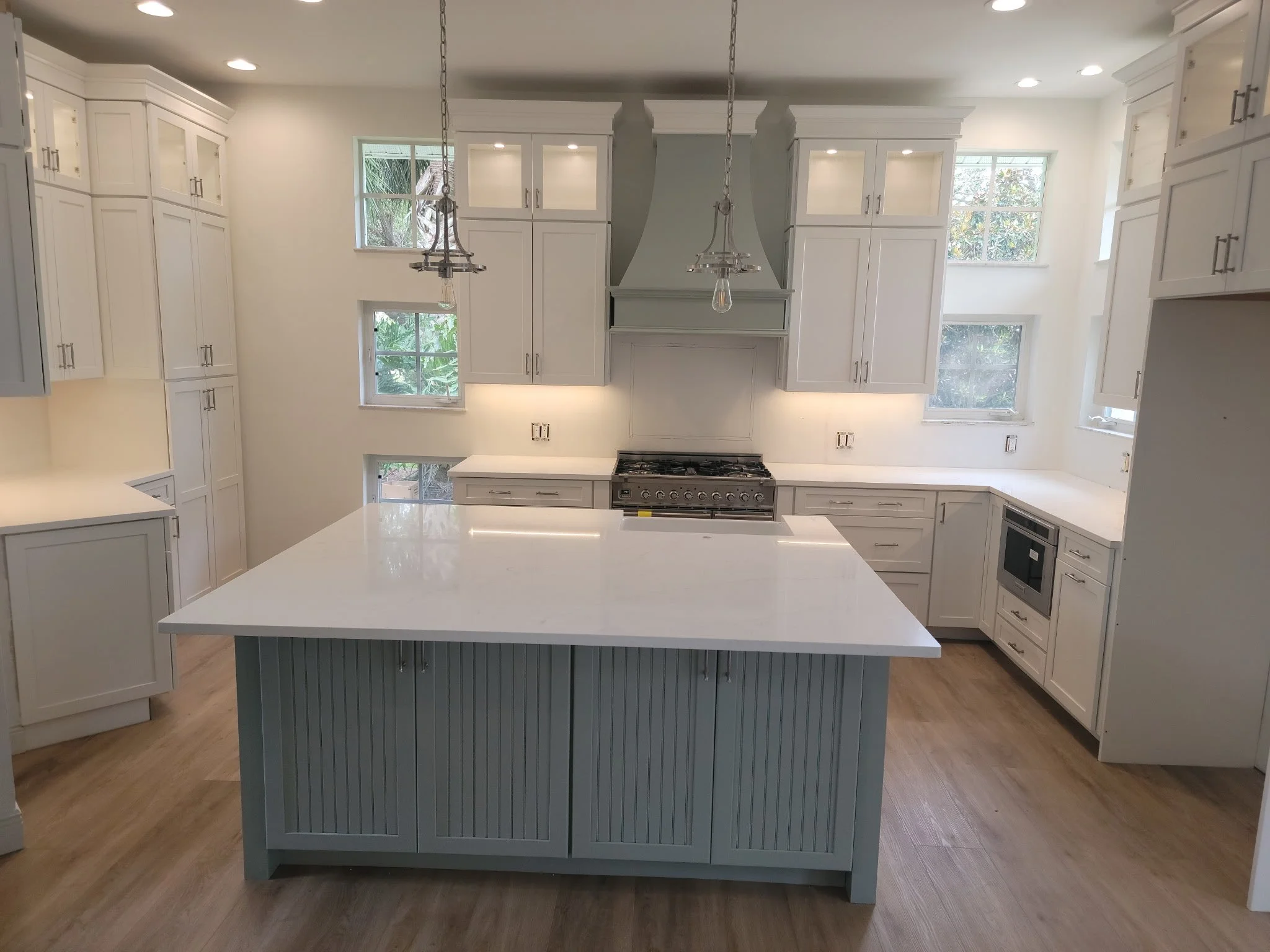Remodeled kitchen in soft sage and white with a big island decorative range hood and pendant lights.