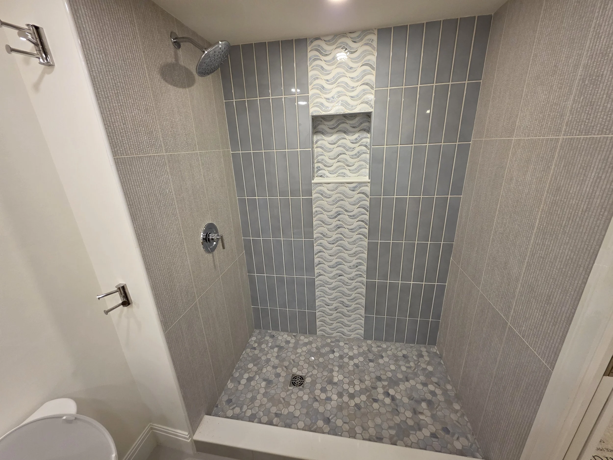 Completed guest shower view 1.  A modern and stylish mix of large and small tiles of soothing colors including a niche and rainfall shower head.