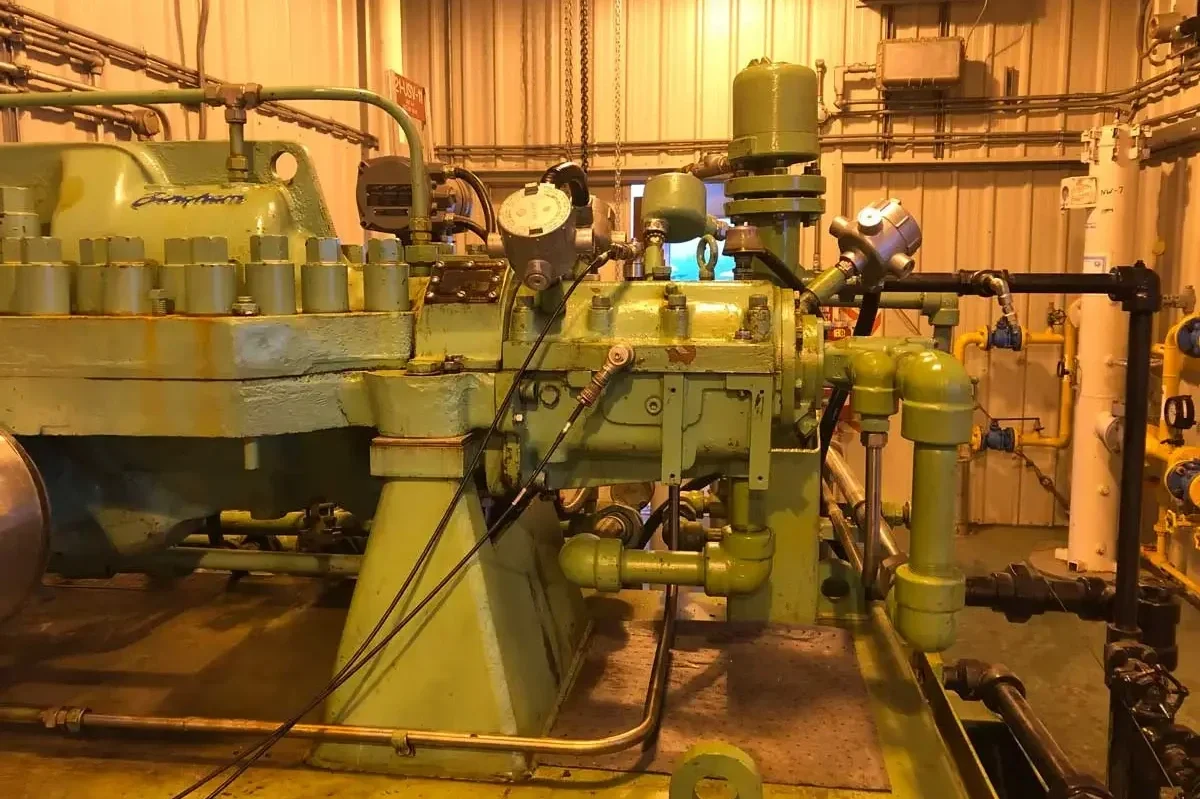 Industrial machinery with green pipes, gauges, and valves inside a metal-walled room.