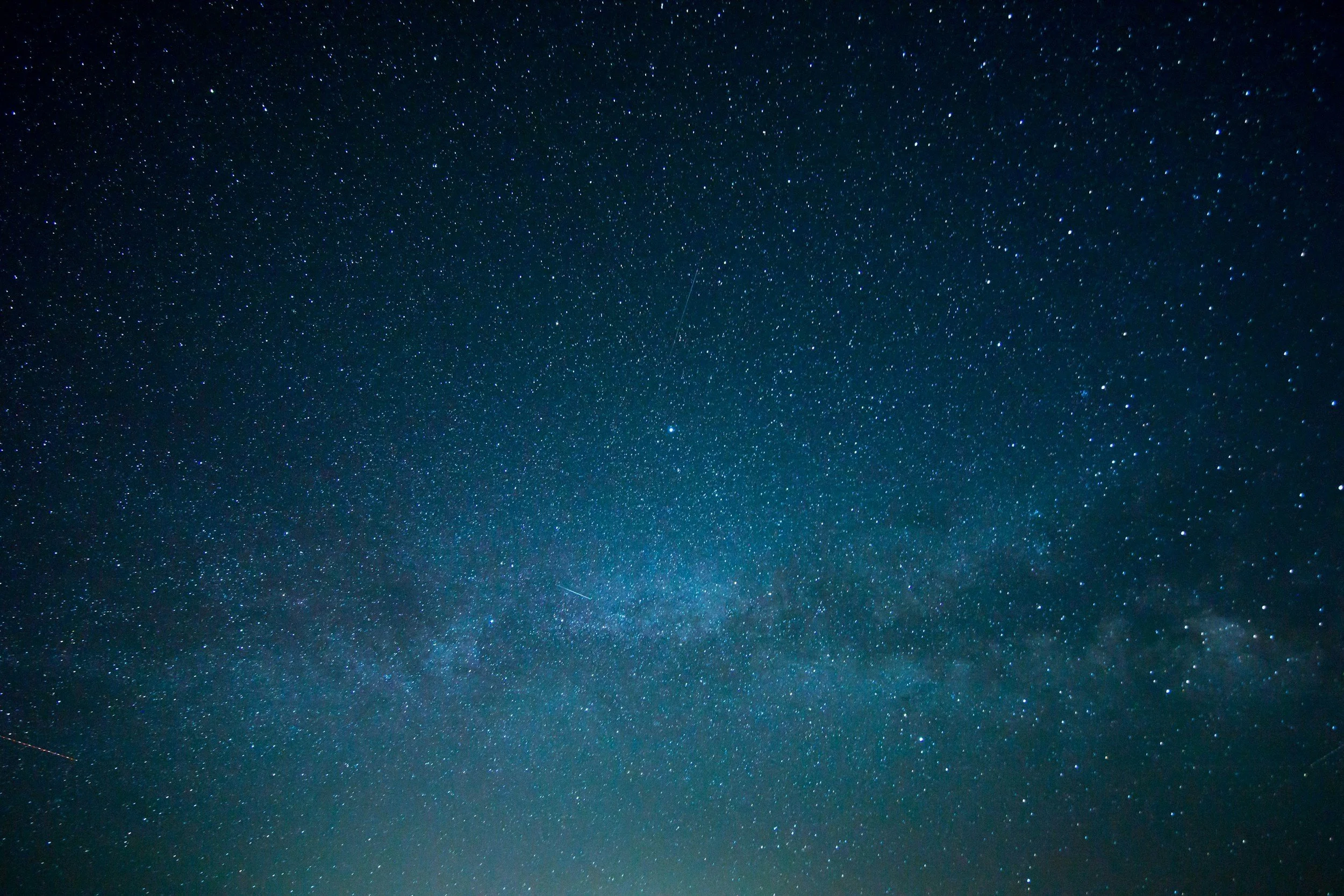 A clear night sky filled with numerous stars and a few streaks of light from shooting stars or satellites.
